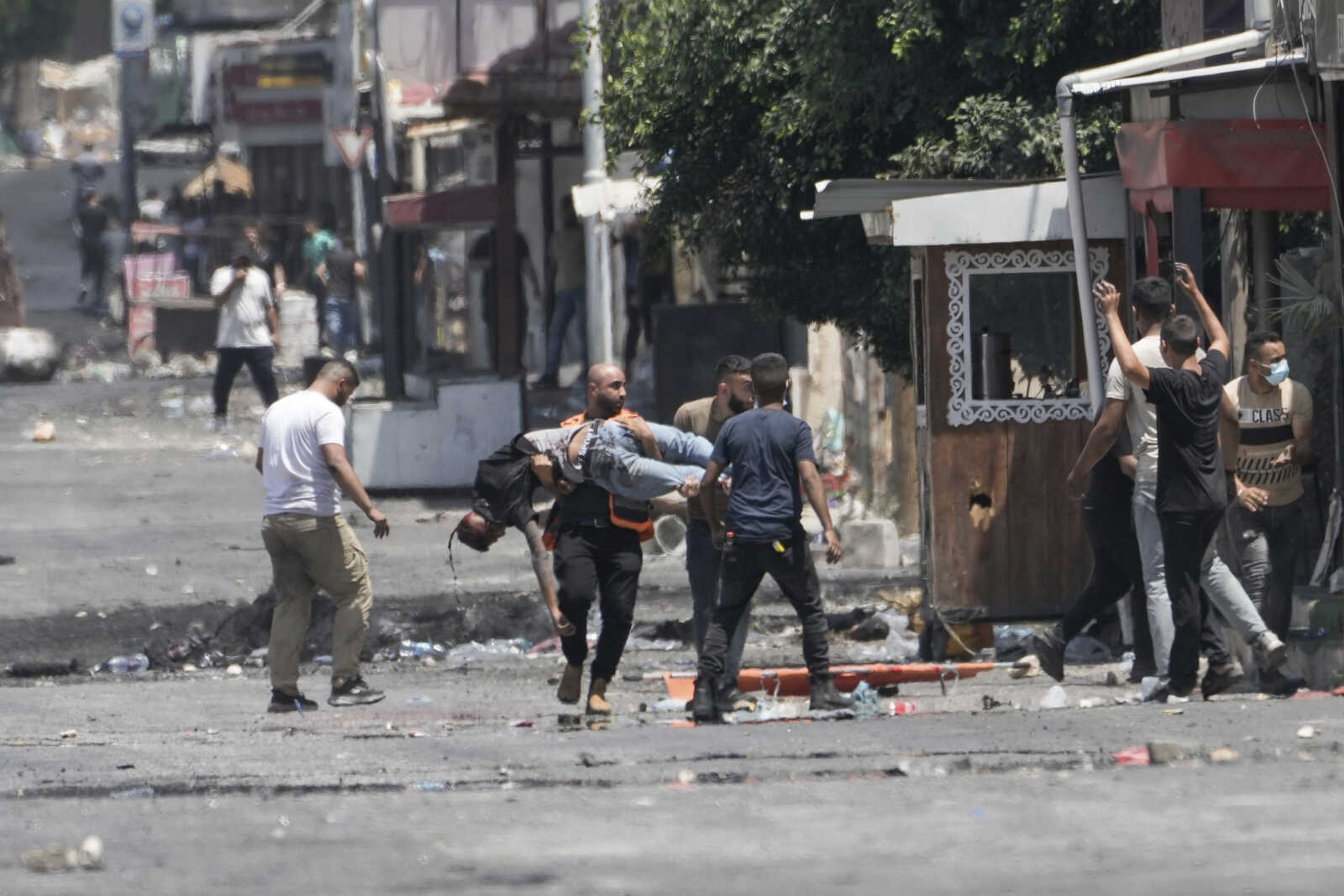 EDS NOTE: GRAPHIC CONTENT - Palestinians carry a wounded man shot by Israeli fire shortly after he threw a bomb toward an Israeli army vehicle during a military raid in the Jenin refugee camp, a militant stronghold in the occupied West Bank, Tuesday, July 4, 2023. Palestinian health officials said at least 10 Palestinians were killed and dozens wounded in the operation, which Israeli forces launched Monday. (AP Photo/Majdi Mohammed)