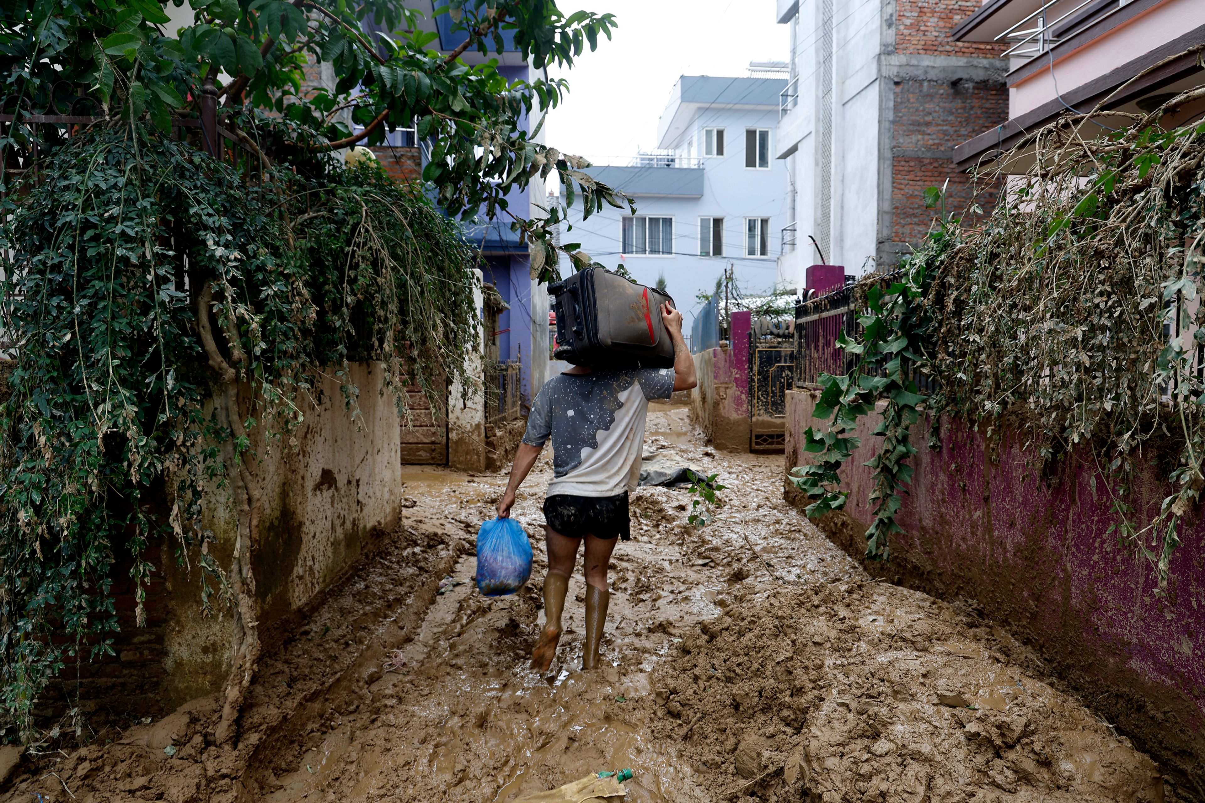 A man walks on a muddy alleyway carrying belongings salvaged from his house in Kathmandu, Nepal, Monday, Sept. 30, 2024 in the aftermath of a flood caused by heavy rains. (AP Photo/Gopen Rai)