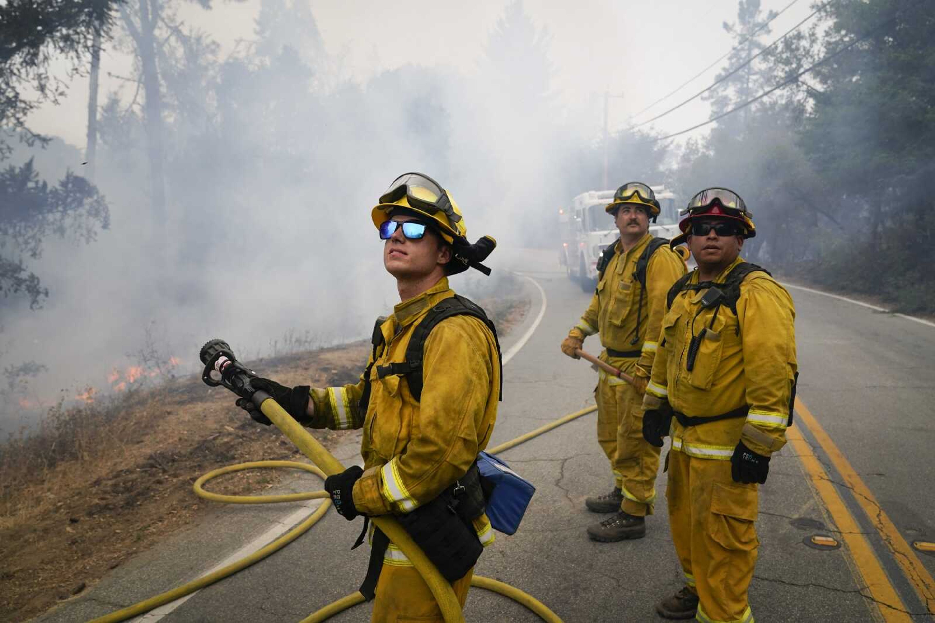 Firefighters Cody Nordstrom, Kyle Harp and Robert Gonzalez, from left, of the North Central Fire station out of Kerman, California, look up at a water-dropping helicopter while fighting the CZU Lightning Complex Fire on Sunday in Bonny Doon, California.