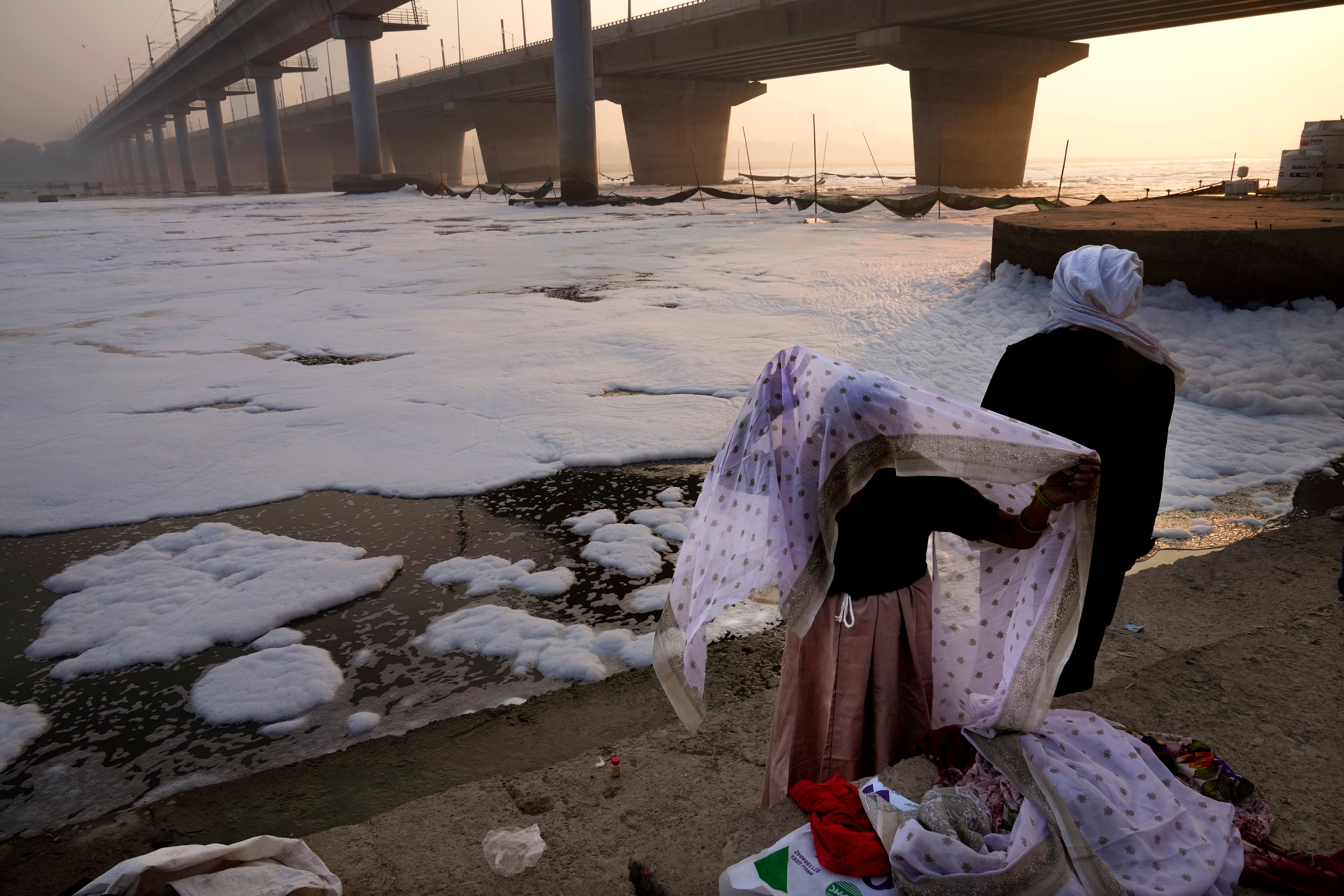 An elderly woman changes her clothes after praying in the river Yamuna filled with toxic foams in New Delhi, India, Tuesday, Oct. 29, 2024. (AP Photo/Manish Swarup)