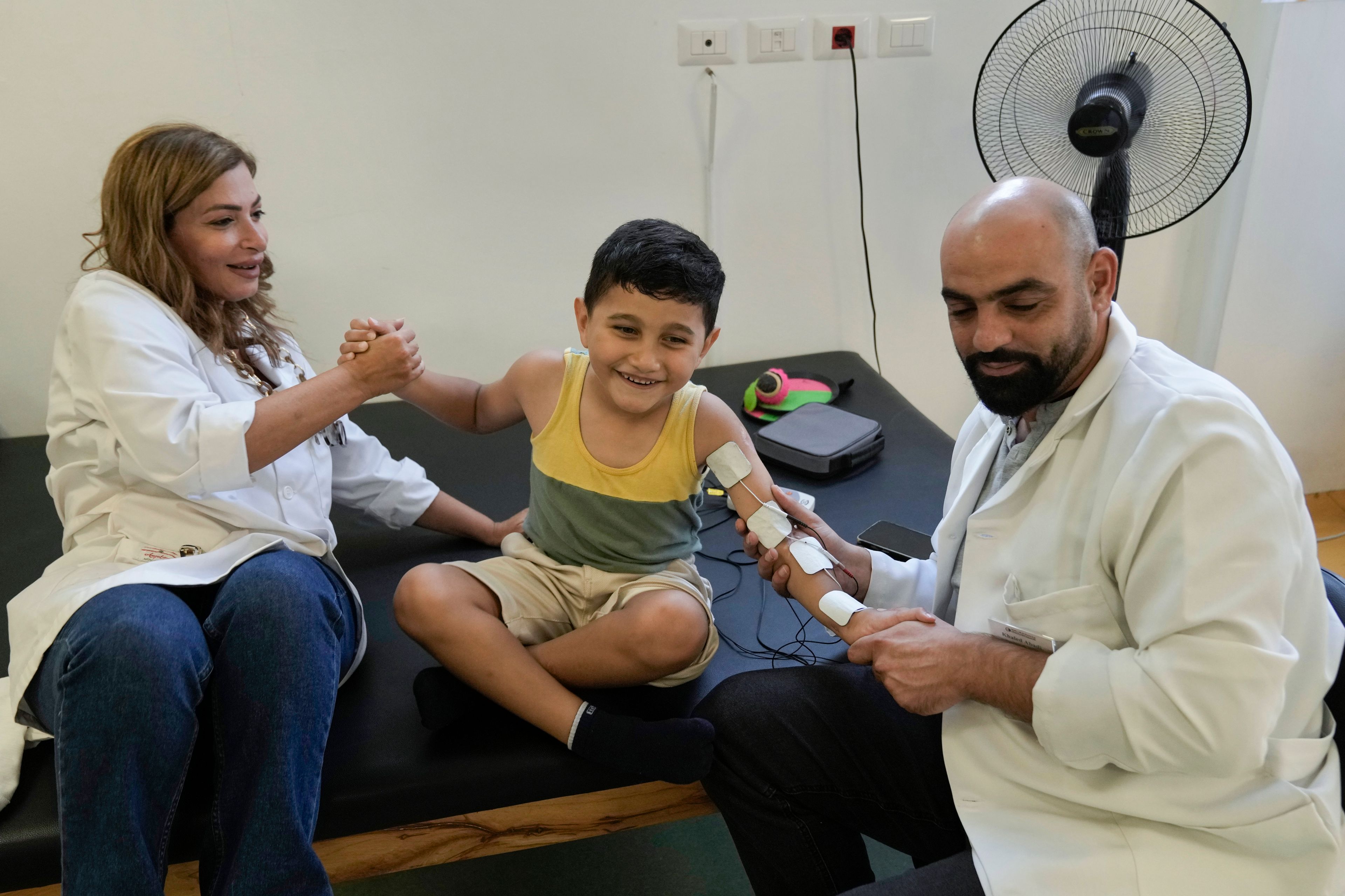 Adam Afana, 5, center, who was brought to Lebanon from the Gaza Strip for treatment after he nearly lost his left arm in an Israeli airstrike that killed his father and sister, receives physiotherapy at a clinic in Mar Elias Palestinian refugee camp in Beirut, Lebanon, Wednesday, Sept. 4, 2024. (AP Photo/Bilal Hussein)