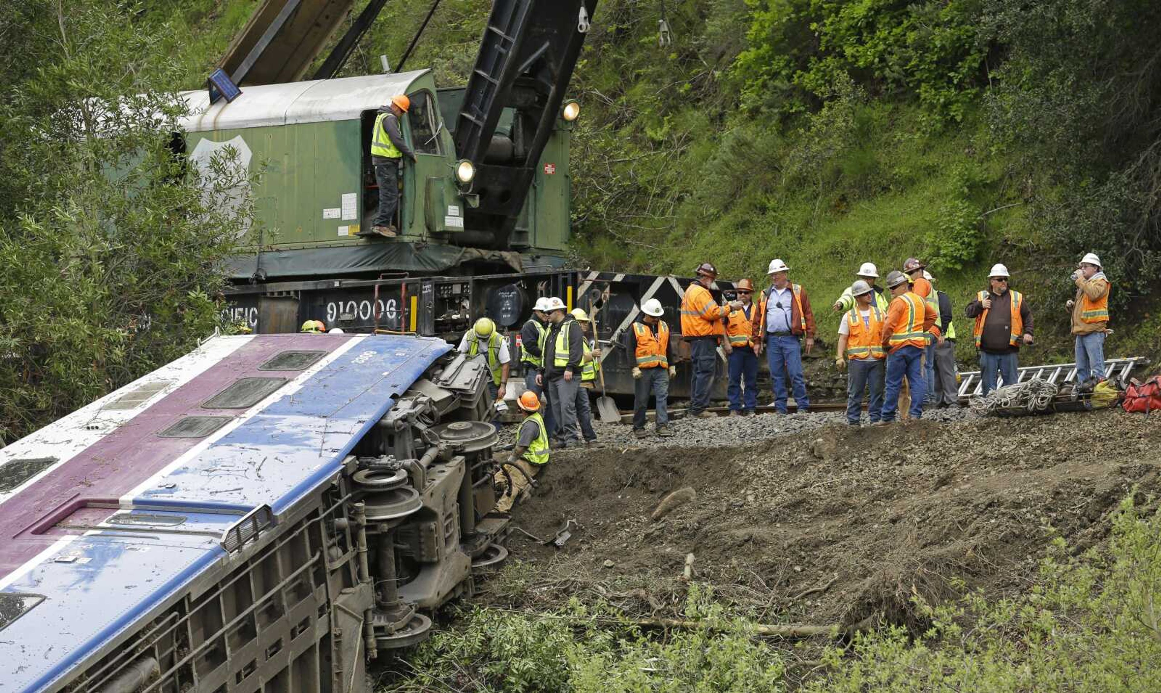 Workers on Tuesday connect a derailed Altamont Corridor Express train to a crane to remove it from Alameda Creek  in Sunol, California.