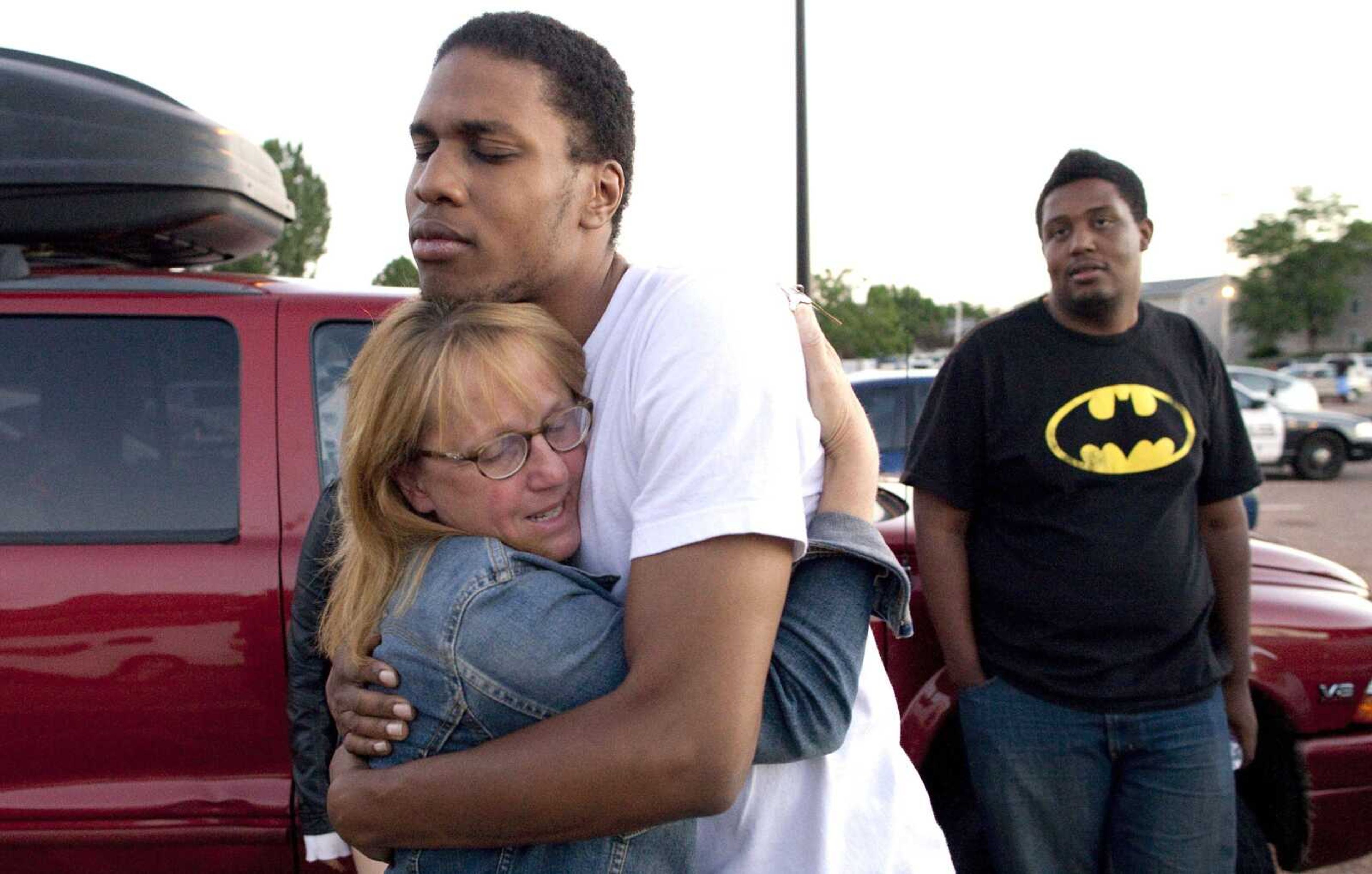 Judy Goos, left, hugs her daughter&#8217;s friend, Isaiah Bow, 20, an eyewitness, as Terrell Wallin, 20, right, looks on, July 20 outside Gateway High School in Aurora, Colo. Witnesses were brought to the school for questioning after a gunman opened fire at the midnight premiere of the &#8220;The Dark Knight Rises&#8221; movie. After fleeing the theater, Bow returned to find his girlfriend safe. &#8220;Very stupid I know, but I didn&#8217;t want to leave her in there,&#8221; Bow said. (Barry Gutierrez ~ Associated Press)