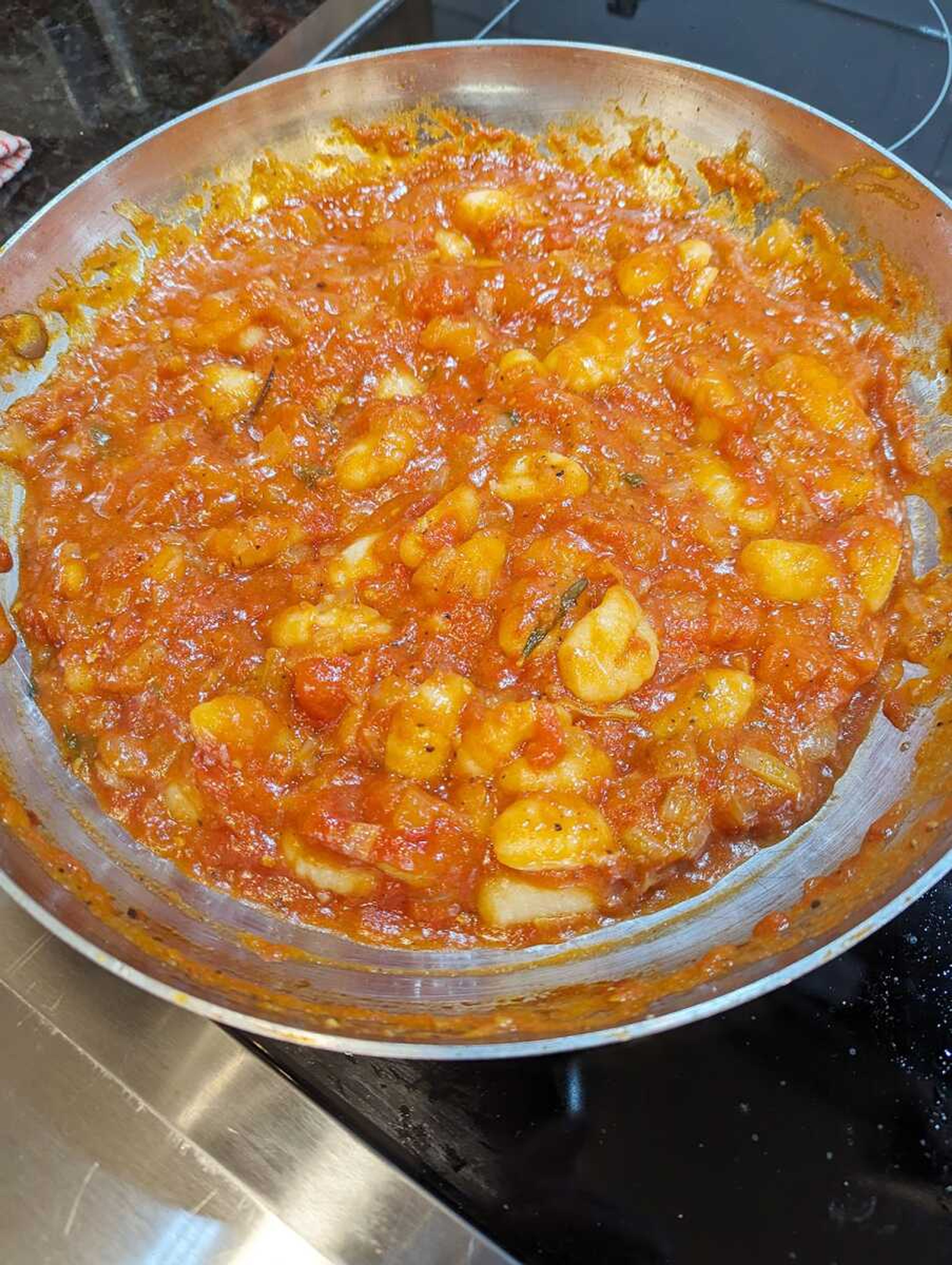 Gnocchi cooked in a sauce made from canned San Marzano tomatoes are ready to be topped with cheese for a dish arguably as good or even better than when made with fresh tomatoes.