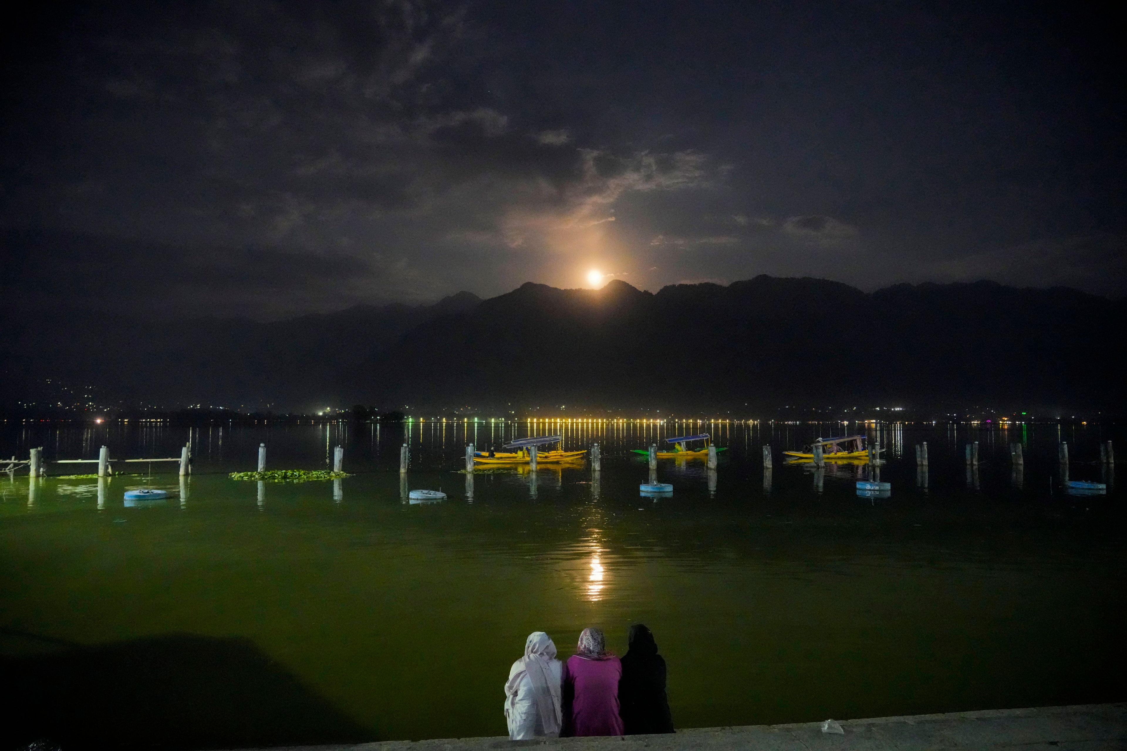 Kashmiri women watch a supermoon rising behind the Zabarwan hills as boatmen row their boats at the Dal Lake on the outskirts of Srinagar, Indian controlled Kashmir, Thursday, Oct. 17, 2024. (AP Photo/Mukhtar Khan)