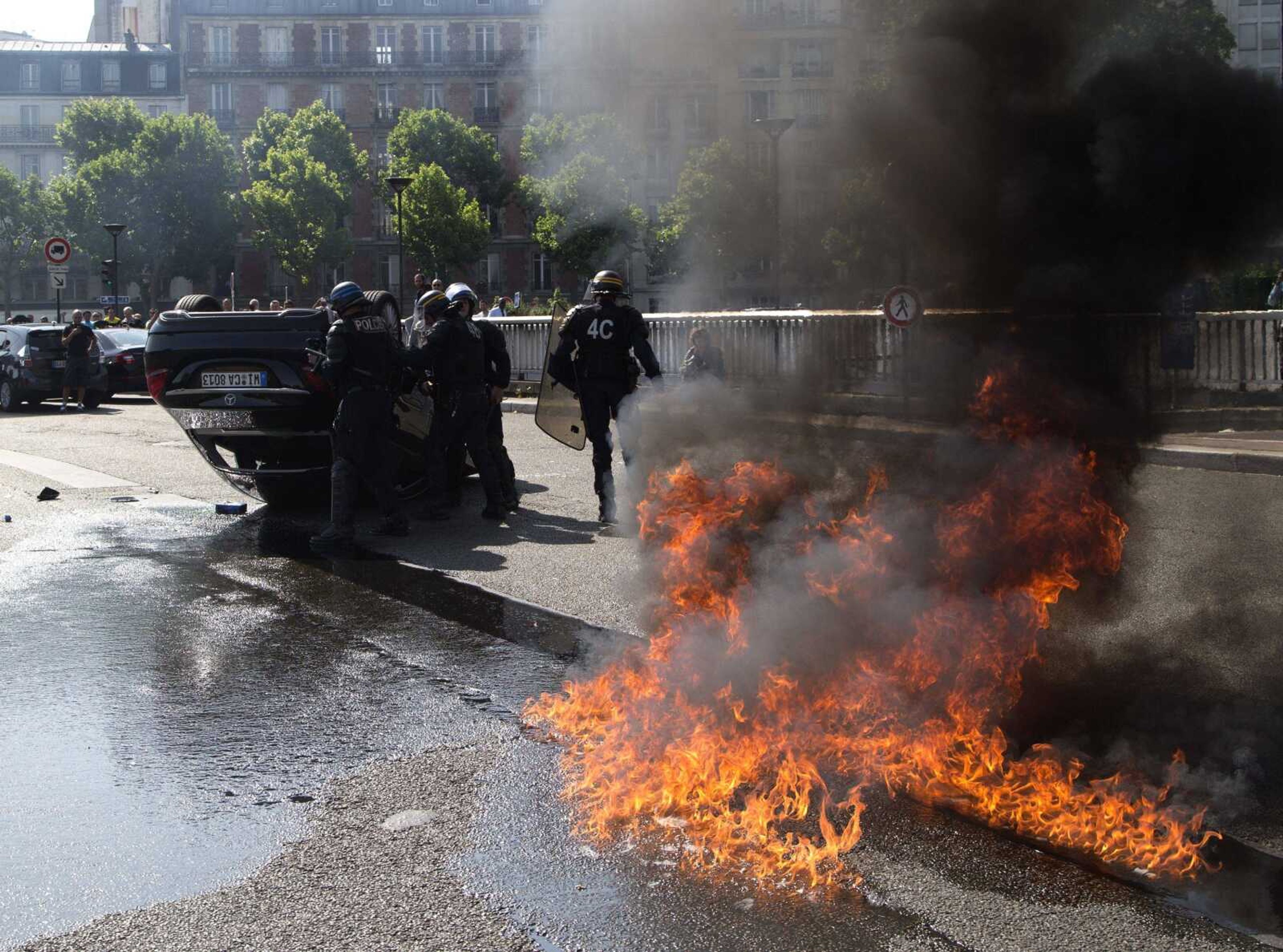 Riot police officers stand by an overthrown car during a taxi drivers demonstration Thursday in Paris. French taxis are on strike around the country, snarling traffic in major cities and slowing access to Paris' Charles de Gaulle airport after weeks of rising and sometimes violent tensions over Uber. (Michel Euler ~ Associated Press)