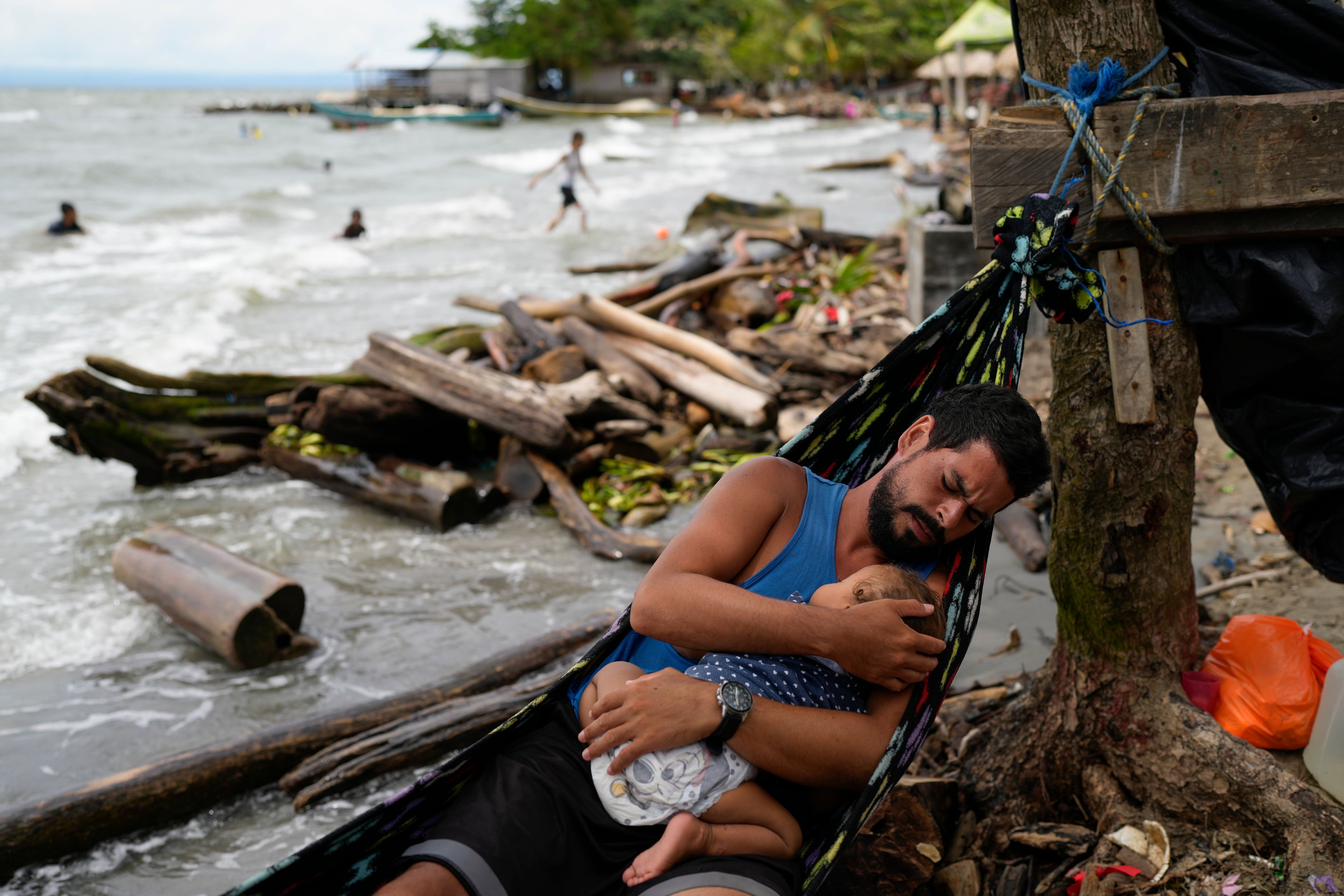 Jackson Vargas, who left Venezuela after the country's disputed election, holds his daughter along the shore in Necocli, Colombia, as they save money ahead of traversing the Darien Gap, Monday, Oct. 14, 2024. (AP Photo/Matias Delacroix)