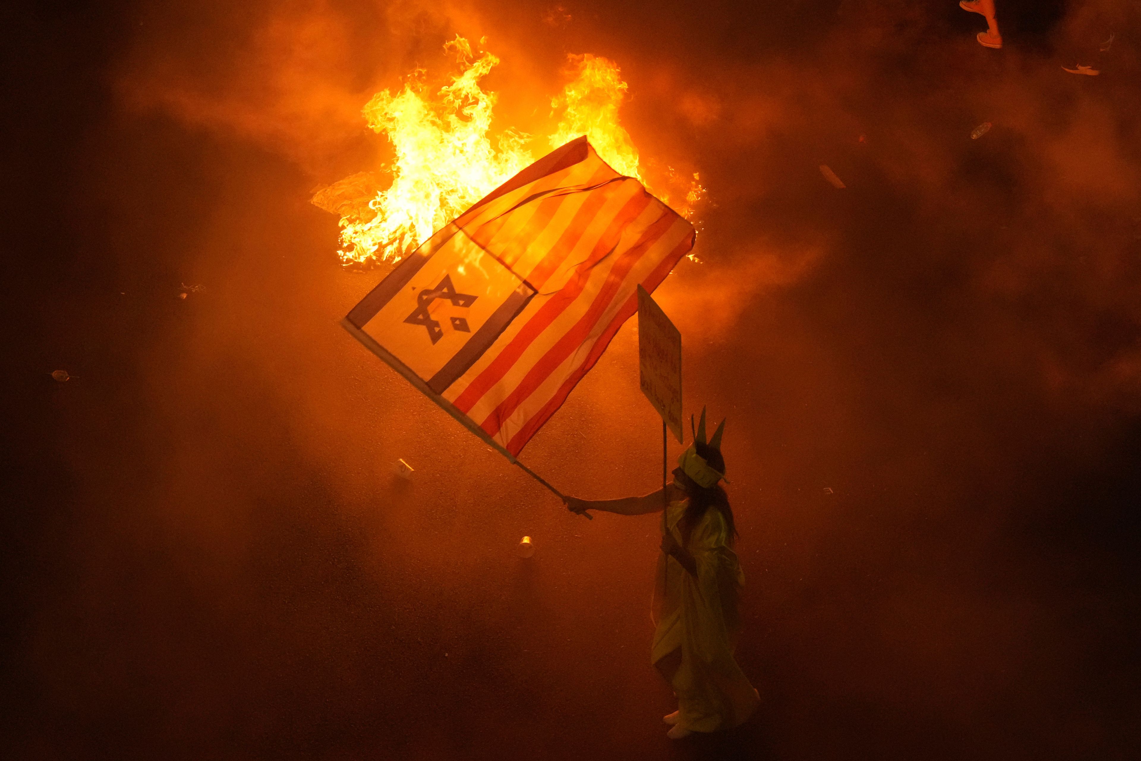 A demonstrator waves the Israeli and U.S. flags during a protest against Prime Minister Benjamin Netanyahu's government and call for the release of hostages held in the Gaza Strip by the Hamas militant group, in Tel Aviv, Israel, Saturday, Sept. 7, 2024. (AP Photo/Ariel Schalit)