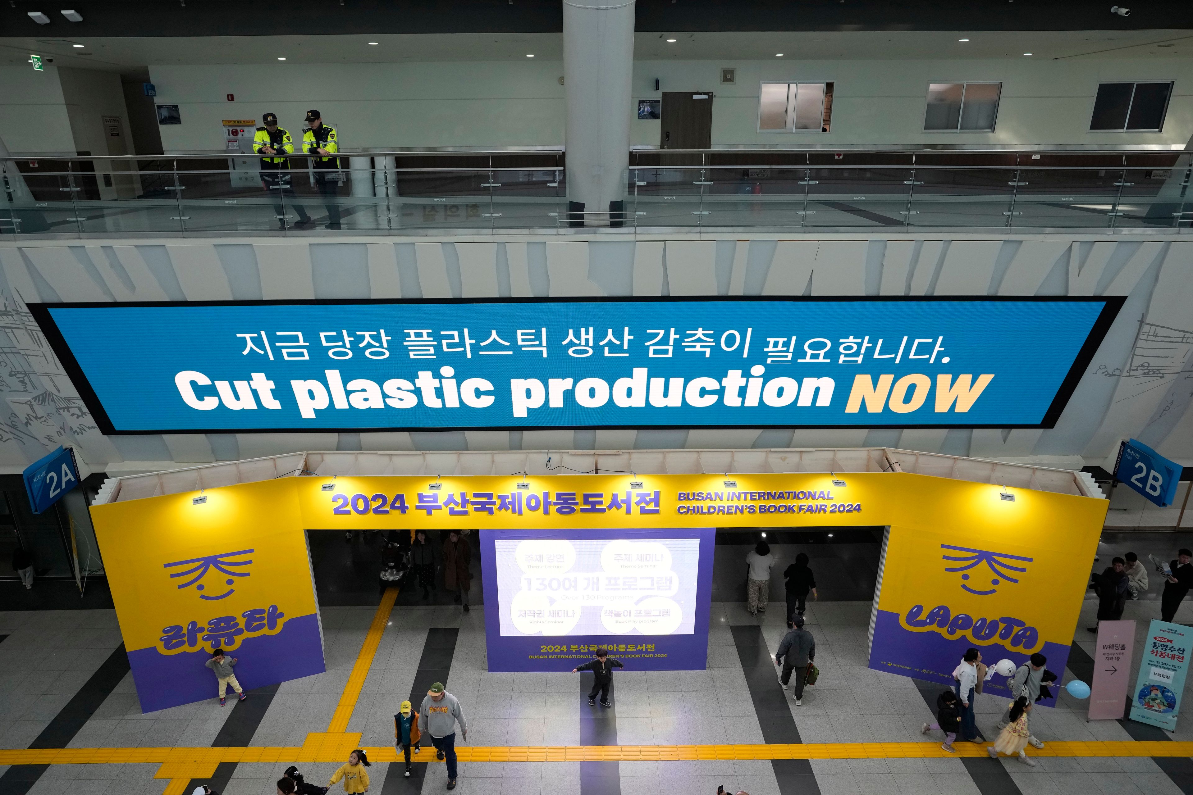 People pass under an electric display board calling for a reduction in plastic production near the venue for the fifth session of the Intergovernmental Negotiating Committee on Plastic Pollution in Busan, South Korea, Sunday, Dec. 1, 2024. (AP Photo/Ahn Young-joon)