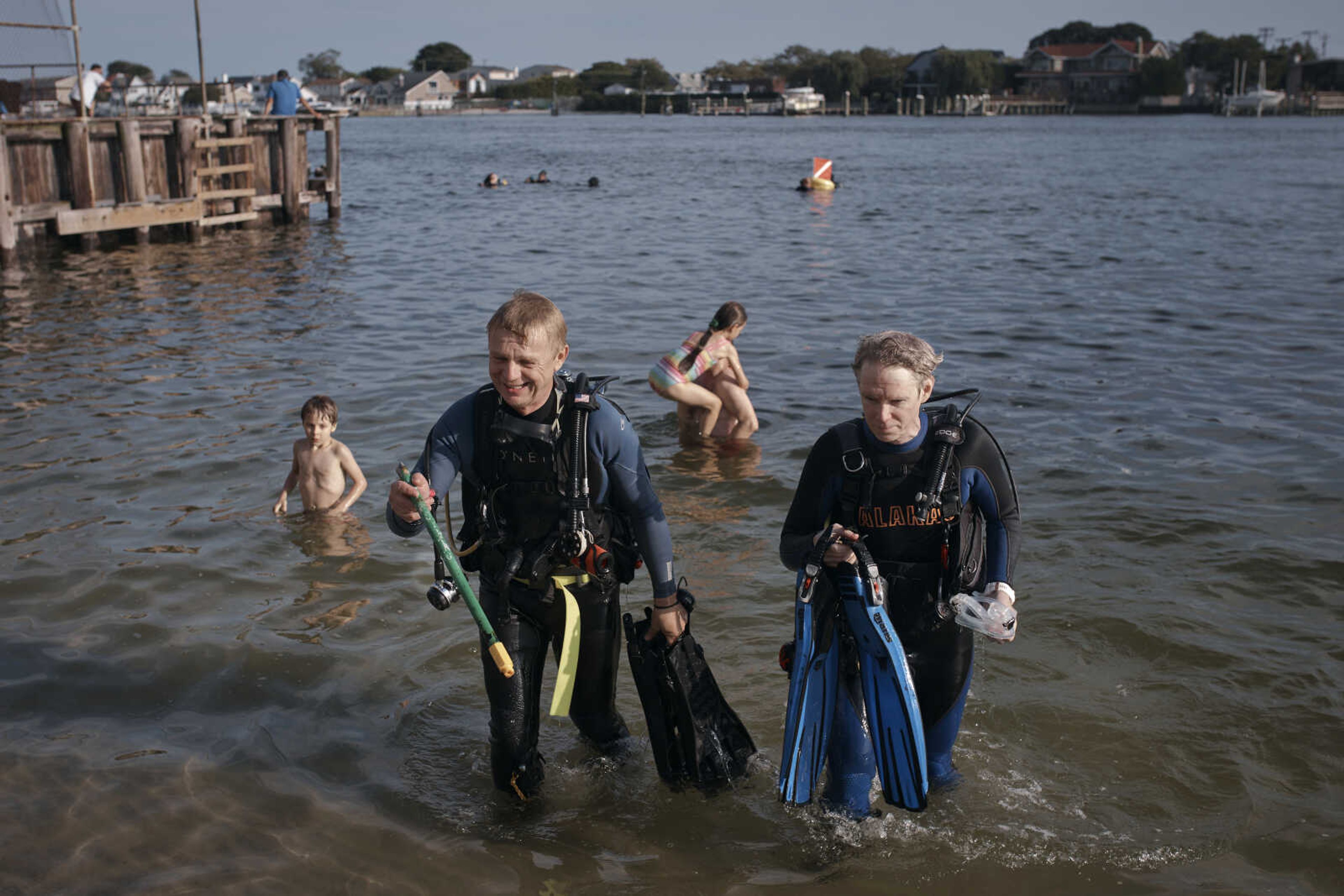 A scuba diver, center left, holds a broken broom handle found as he comes out of the water with his colleague, center right, during an underwater cleanup Aug. 27 in the Queens borough of New York. A diving group takes part in a monthly cleanup at a cove in the community of Far Rockaway, about 4 miles south of John F. Kennedy Airport, to help the global effort to undo ocean pollution.