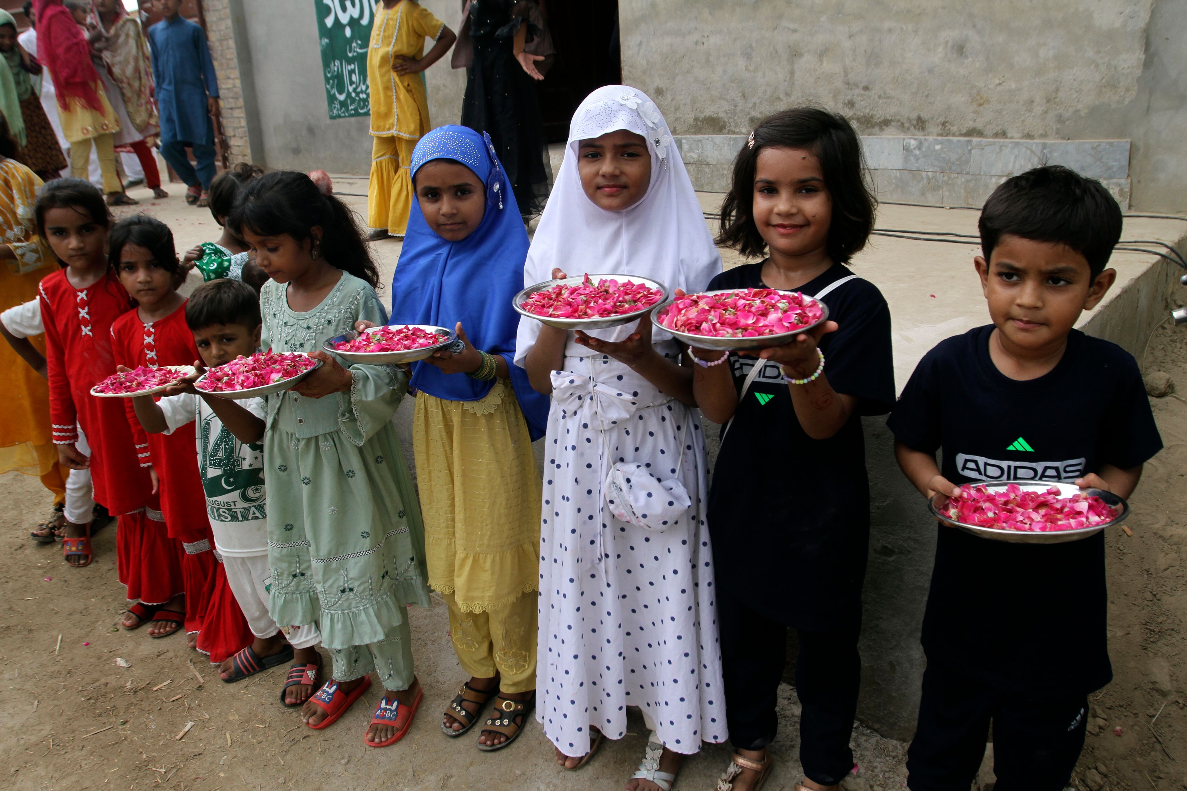 Children of the family of Arshad Nadeem, javelin gold medalist, hold flowers outside his house for his welcome reception, in Mian Channu, Khanewal district, of Pakistan, Sunday, Aug. 11, 2024. (AP Photo/Asim Tanveer)