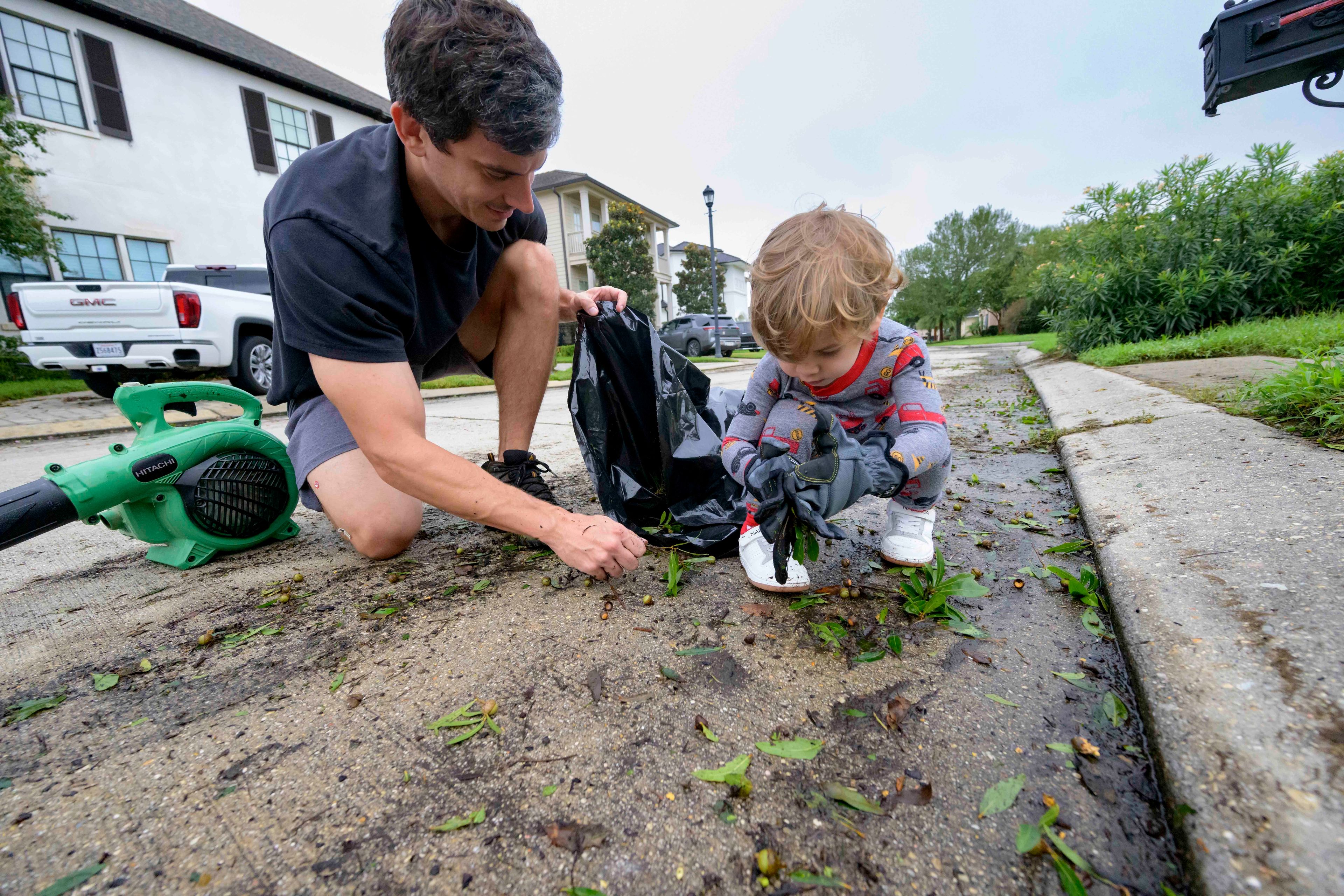 John Finney and his son Gabriel, 2, using gloves, clean up debris after Hurricane Francine near their home in Kenner, La., in Jefferson Parish, Thursday, Sept. 12, 2024. (AP Photo/Matthew Hinton)