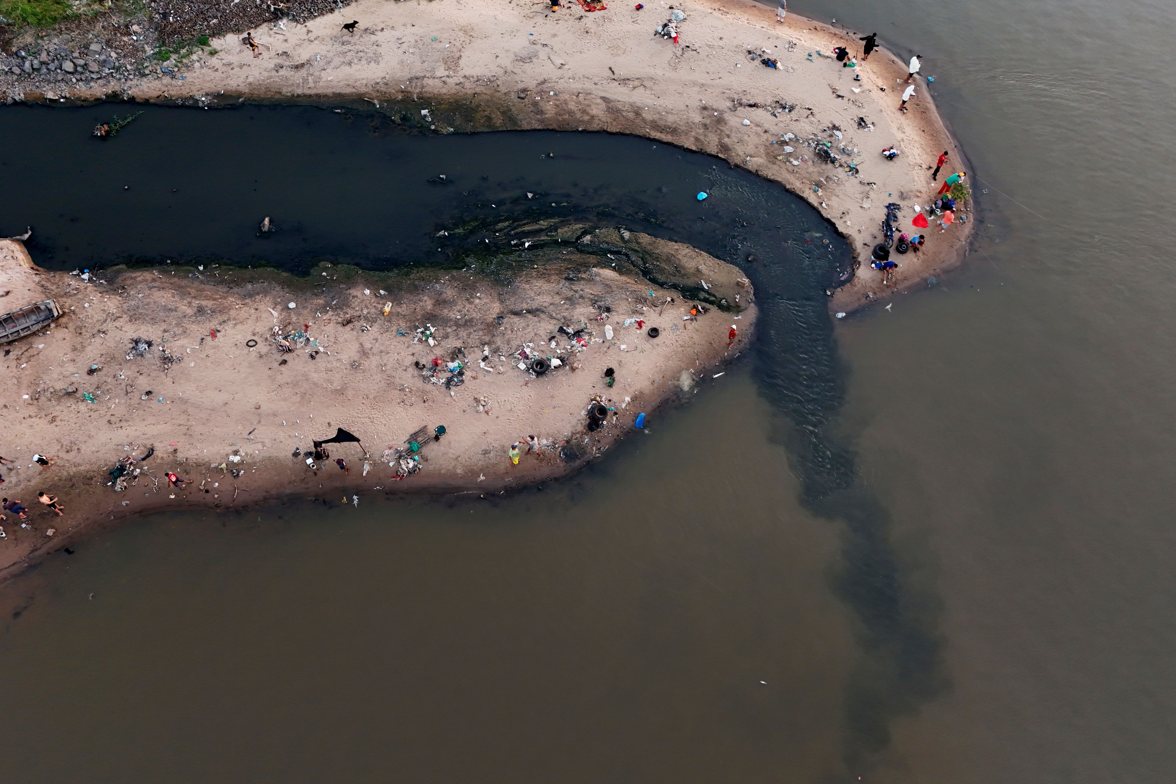 People fish next to drainage that flows into the Paraguay River in Asuncion, Paraguay, on Jan. 28, 2024. (AP Photo/Jorge Saenz)