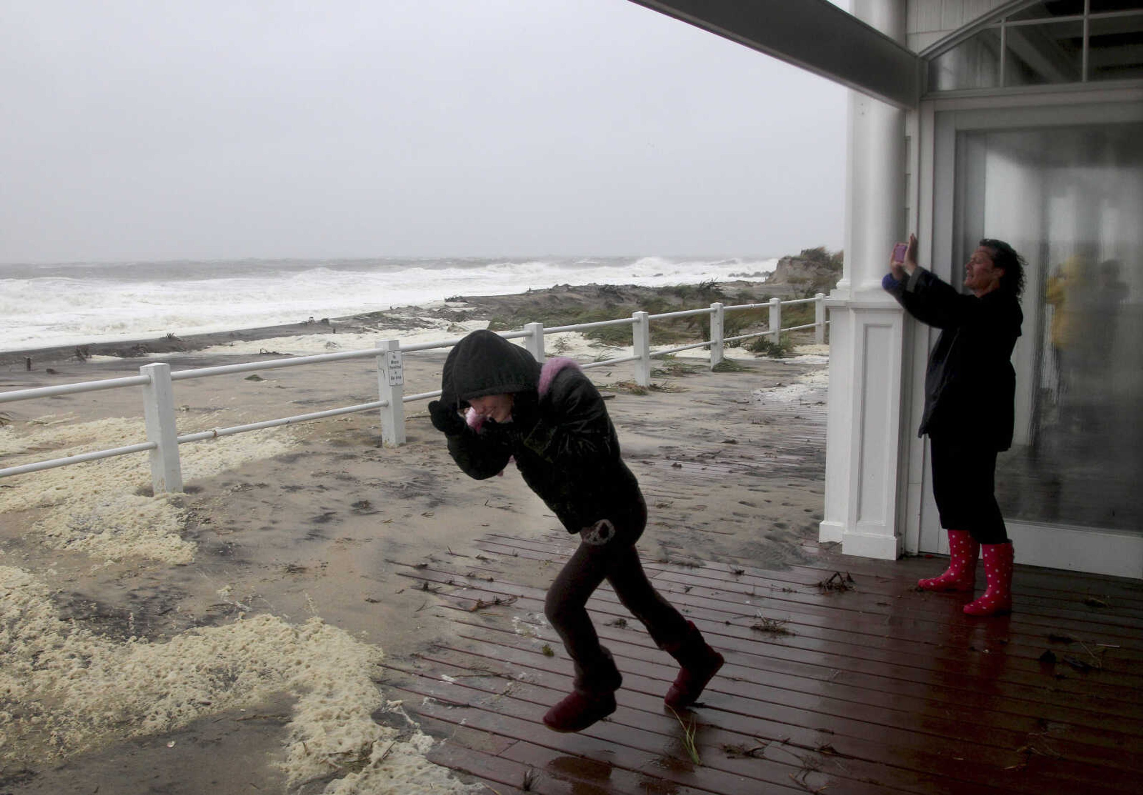 Madison Maher, left, runs out into the rain and wind while her mother, Susan Sorenson, takes a picture of the rough surf in Sea Bright, N.J., Monday, Oct. 29, 2012. Hurricane Sandy continued on its path Monday, as the storm forced the shutdown of mass transit, schools and financial markets, sending coastal residents fleeing, and threatening a dangerous mix of high winds and soaking rain.   (AP Photo/Seth Wenig)