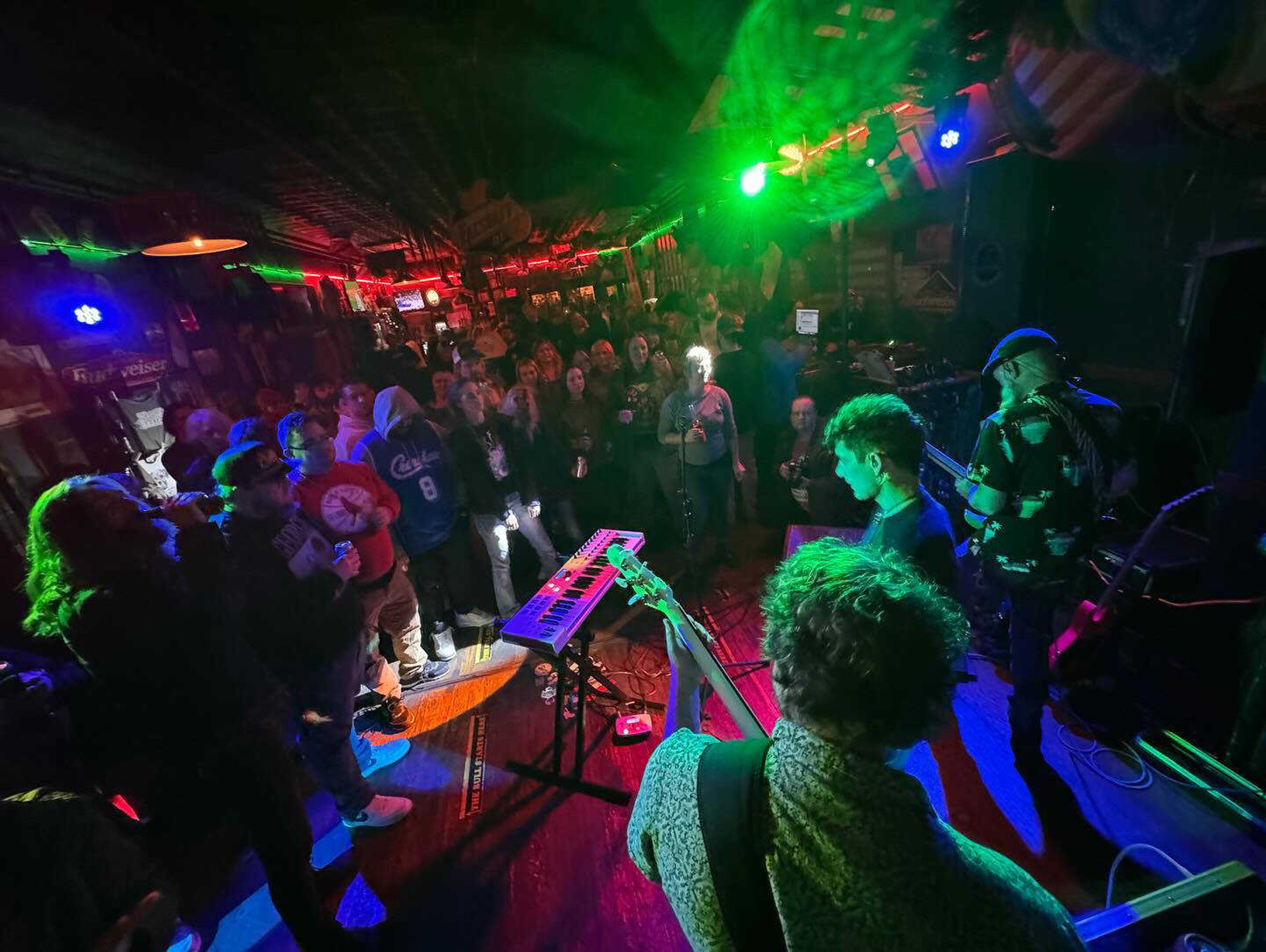 A crowd watches the band Noir Daze close out the CGMO Rock Show at The Rude Dog Pub on February 10, 2024. Nik Scarpaci, Nate Comer and George Adams from Noir Daze are pictured playing.