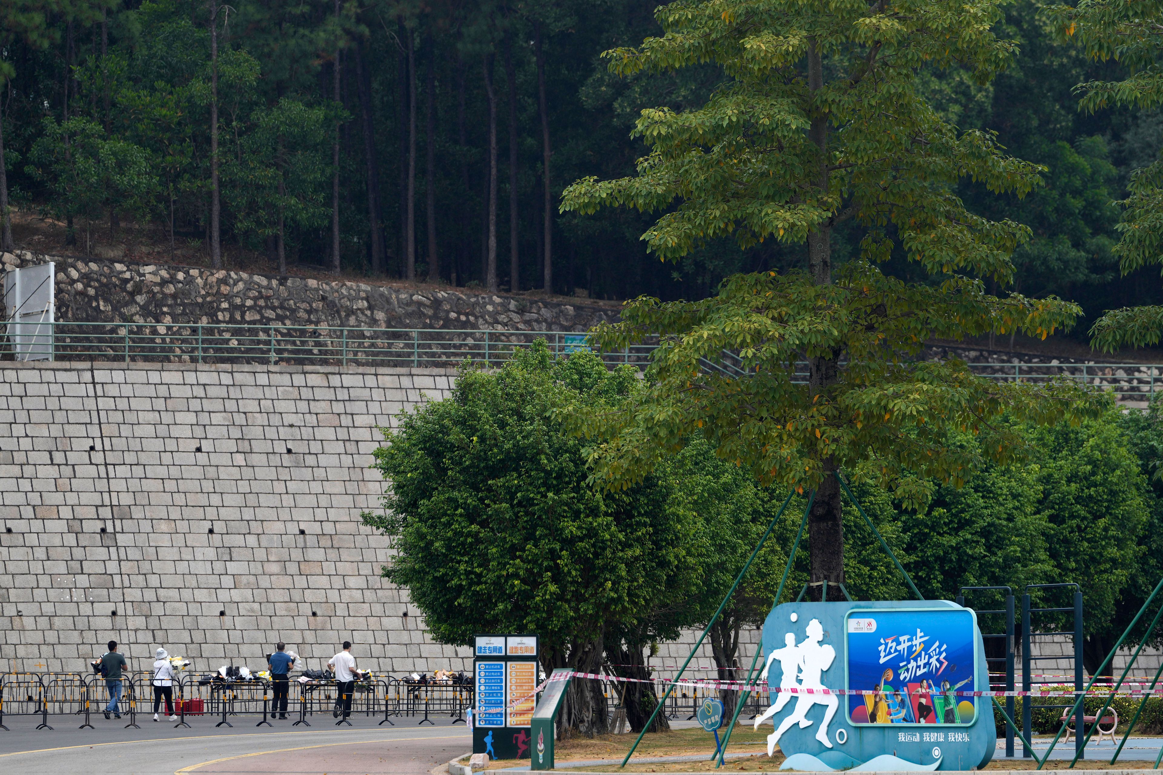 Volunteers relocate flowers laid outside "Zhuhai People's Fitness Plaza" to a barrier leading into the area where a man rammed his car into people exercising at the sports center, in Zhuhai in southern China's Guangdong province on Wednesday, Nov. 13, 2024. (AP Photo/Ng Han Guan)