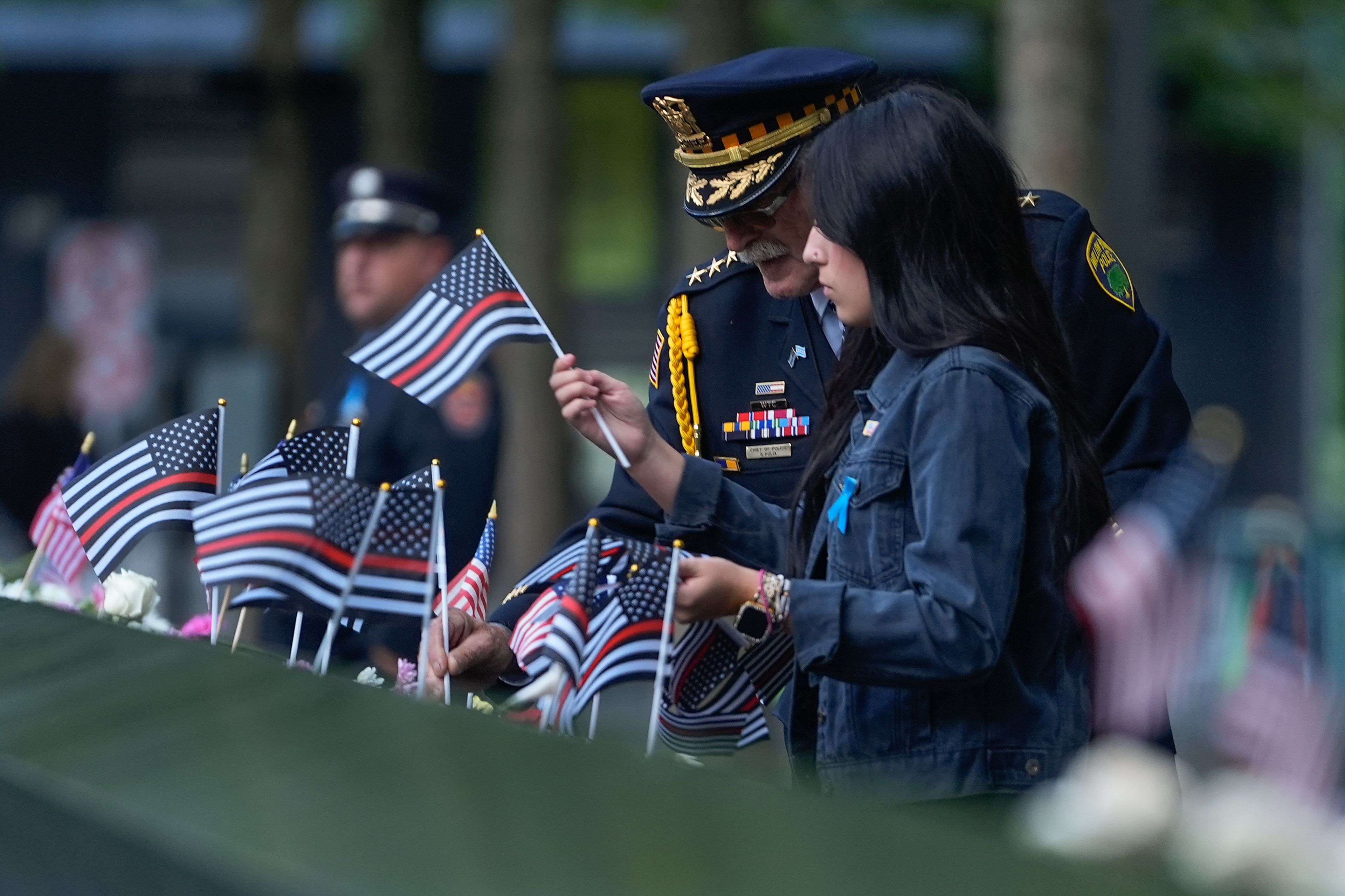 Sam Pulia, left, Willow Springs, Ill police chief, places flags on the bronze parapets at the 9/11 Memorial on the 23rd anniversary of the Sept. 11, 2001 attacks, Wednesday, Sept. 11, 2024, in New York. (AP Photo/Pamela Smith)