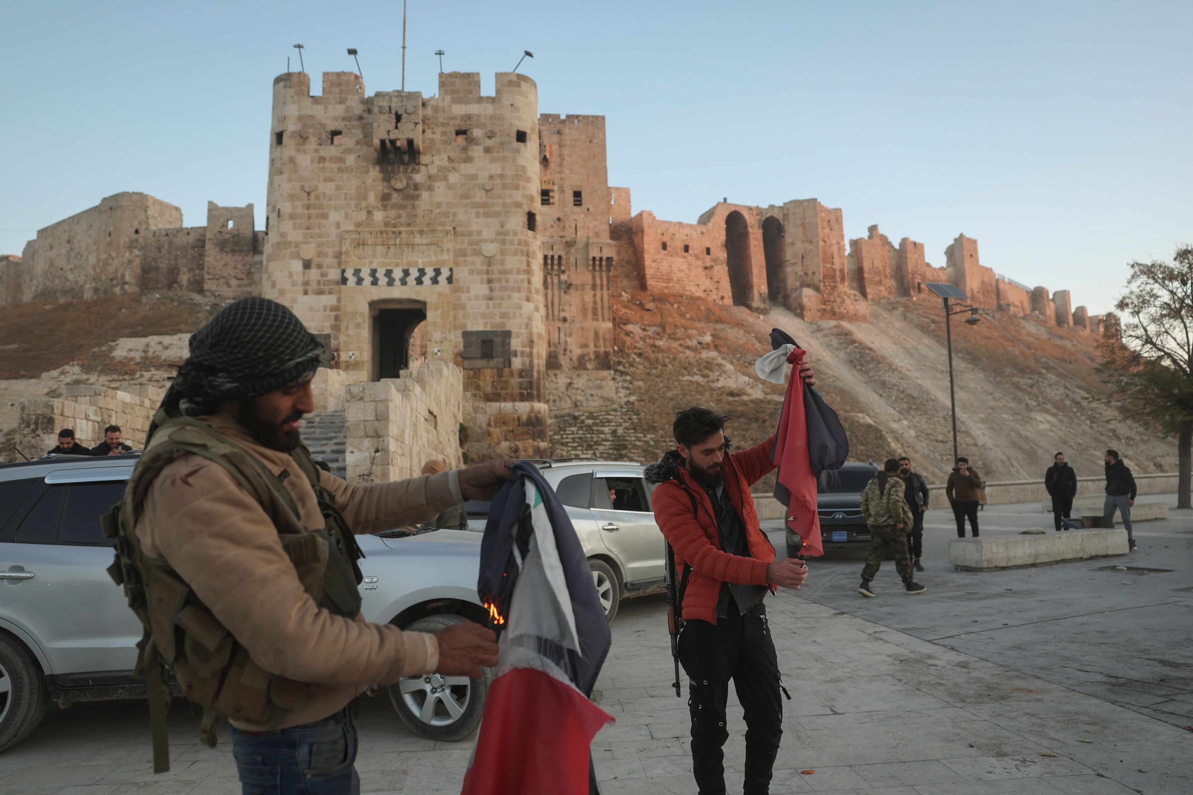 Syrian opposition fighters burn government Syrian flags for the cameras next to Aleppo's old city, Saturday Nov. 30, 2024. (AP Photo/Ghaith Alsayed)