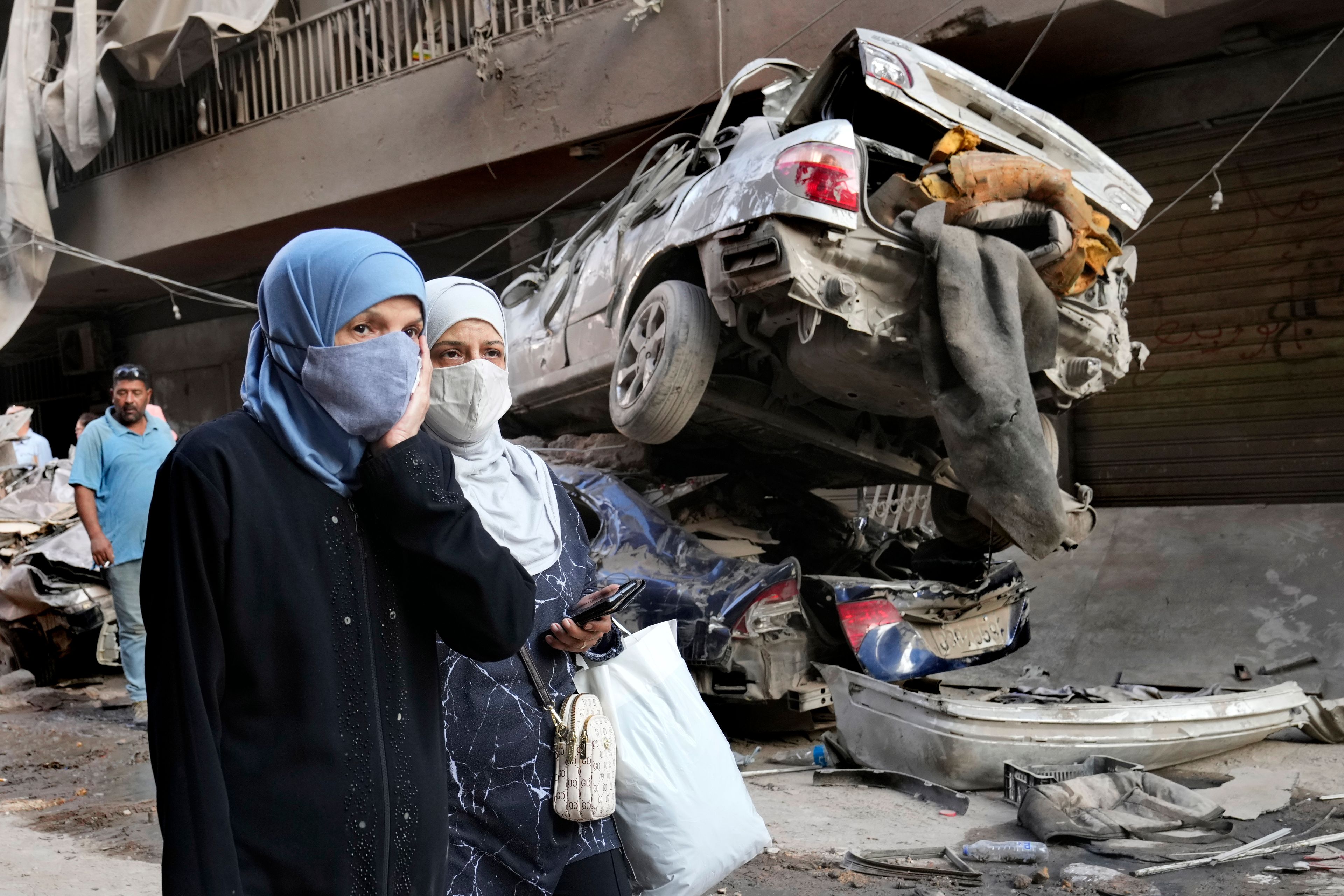 Lebanese women pass near destroyed cars, at the site of Thursday's Israeli airstrike, in Beirut, Lebanon, Friday, Oct. 11, 2024. (AP Photo/Hussein Malla)