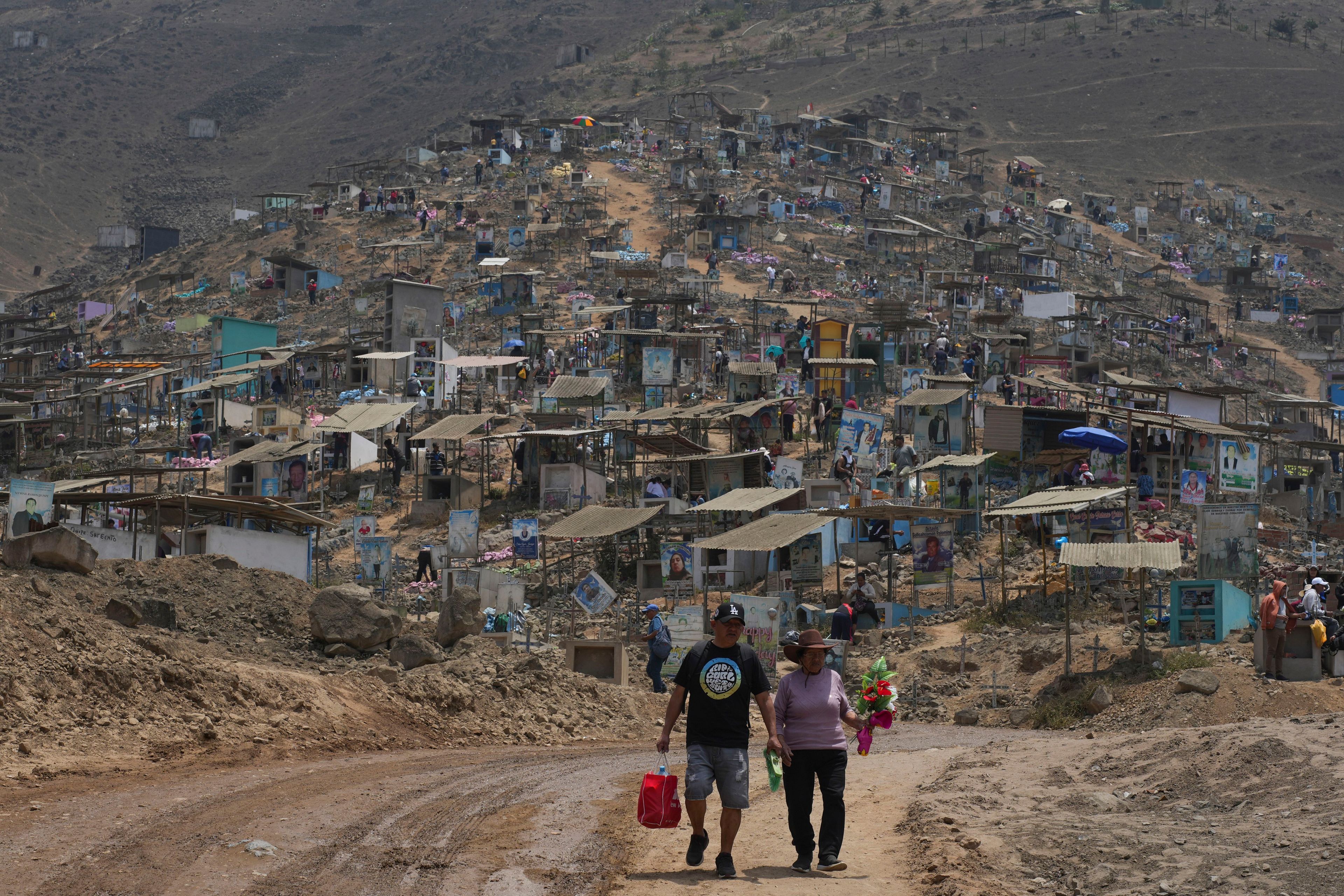 A couple arrive to the Nueva Esperanza cemetery to decorate family graves marking the Day of the Dead, in the Villa Maria community of Lima, Peru, Friday, Nov. 1, 2024. (AP Photo/Guadalupe Pardo)