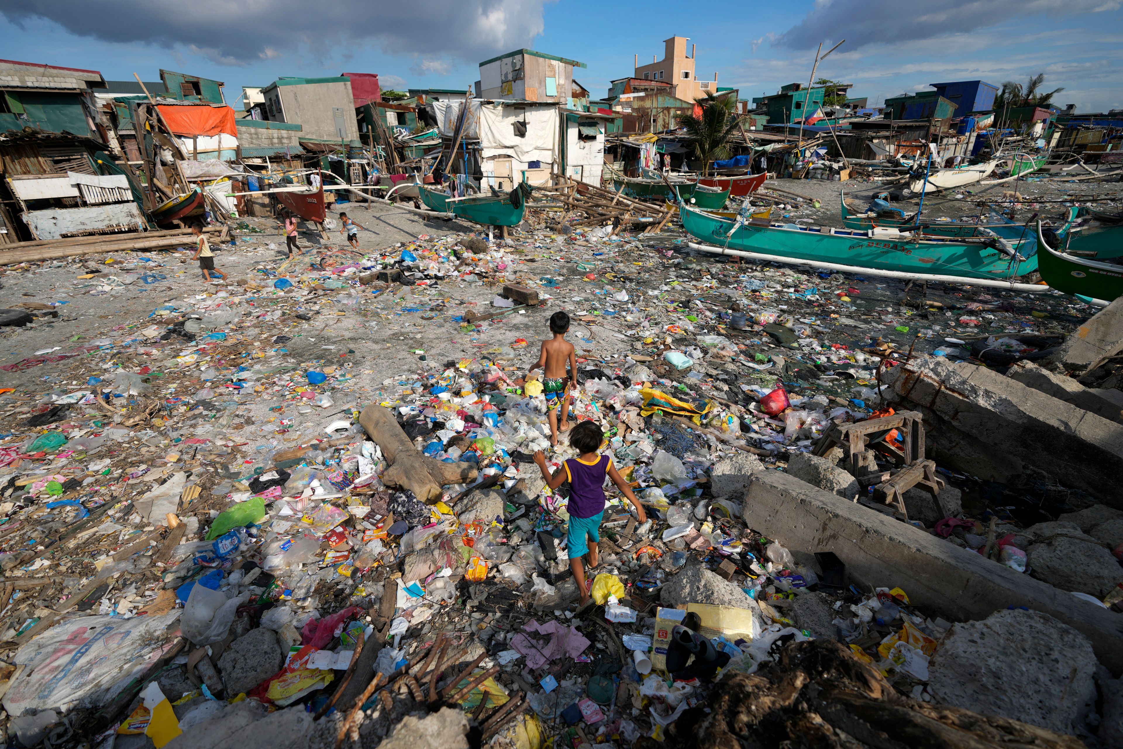 Children walk along debris, including plastics, that was washed ashore from previous typhoons along a bayside slum area on Tuesday, Nov. 26, 2024, in Navotas, Philippines. (AP Photo/Aaron Favila)