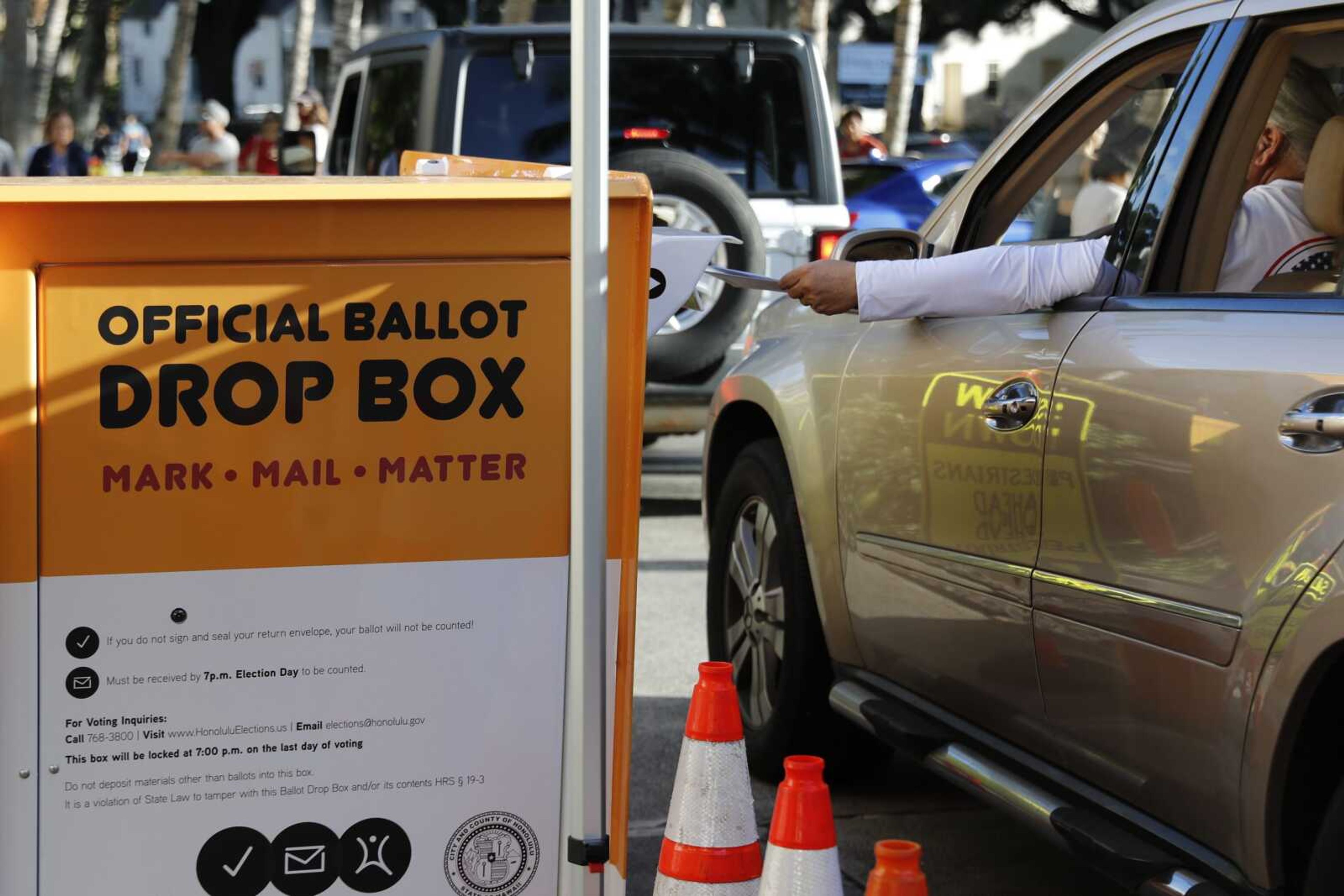 A driver slides a ballot into a voting drop box location Tuesday in Honolulu.