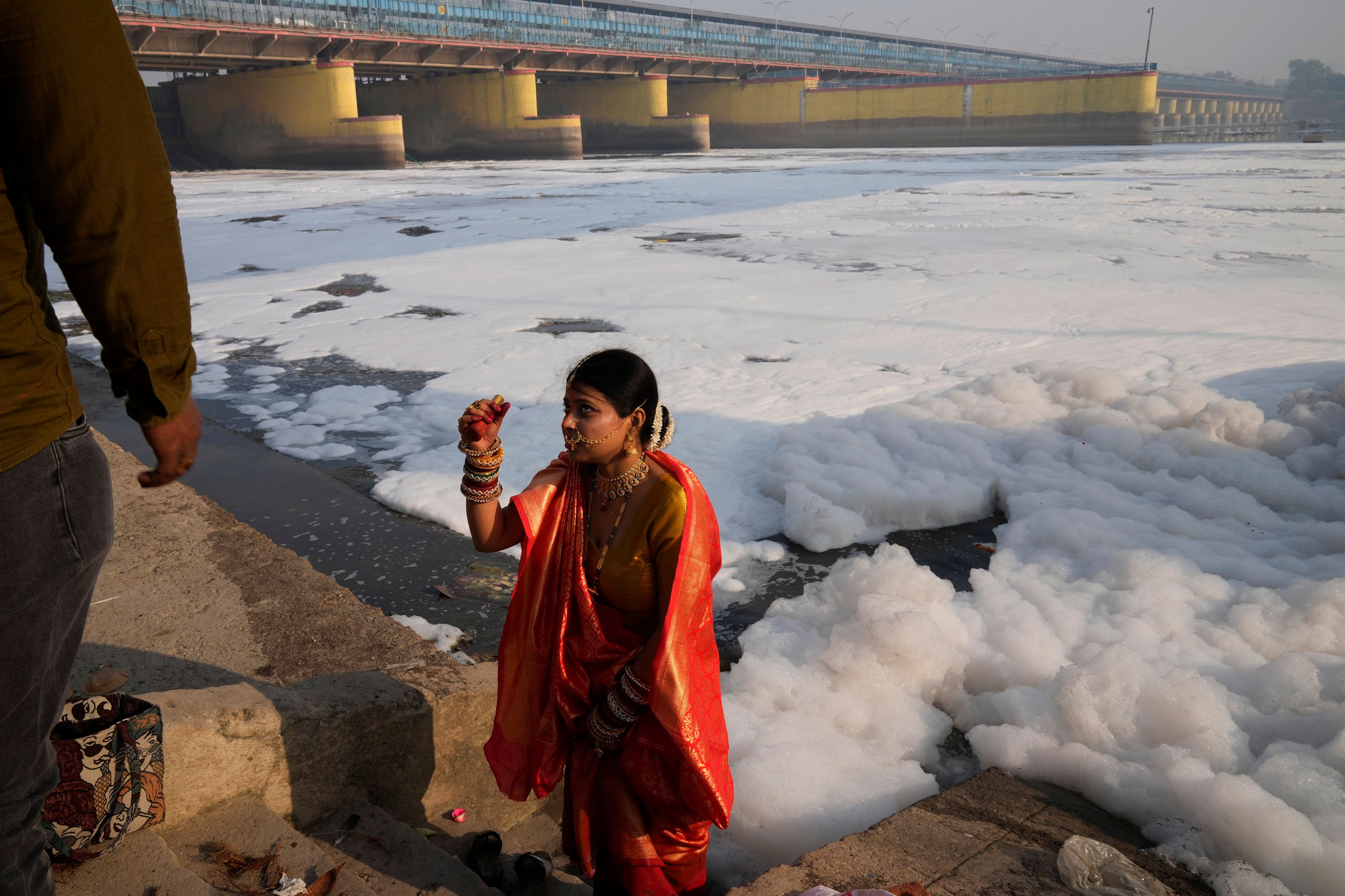 A woman in traditional attire gets photographed in front of the river Yamuna filled with toxic foams in New Delhi, India, Tuesday, Oct. 29, 2024. (AP Photo/Manish Swarup)