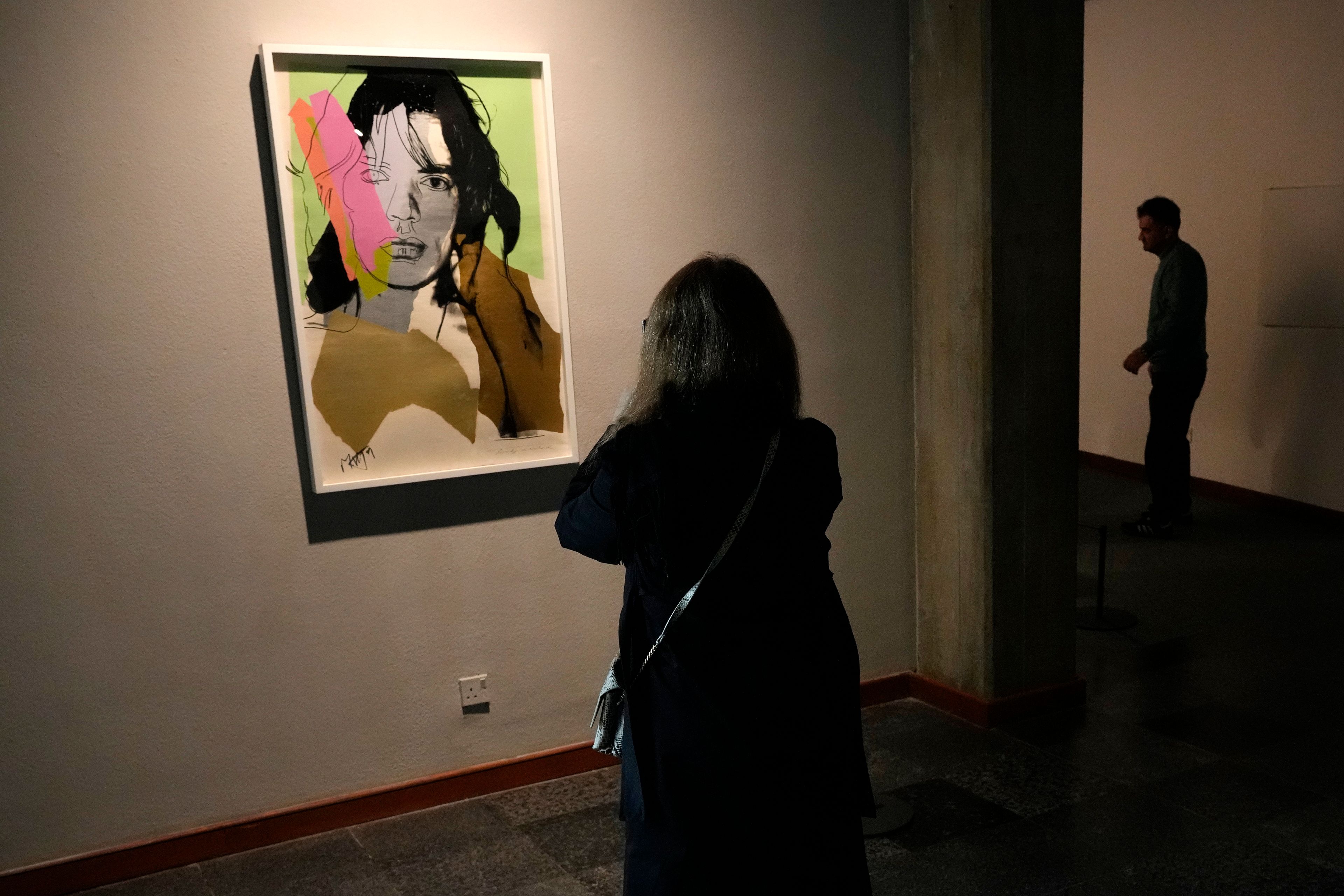 A woman takes a snapshot of a portrait of Rolling Stones frontman Mick Jagger by American artist Andy Warhol as she visits an exhibition titled Eye to Eye which showcases over 120 works by modern world artists as well as Iranian painters at Tehran Museum of Contemporary Art, in Tehran, Thursday, Nov. 21, 2024. (AP Photo/Vahid Salemi)