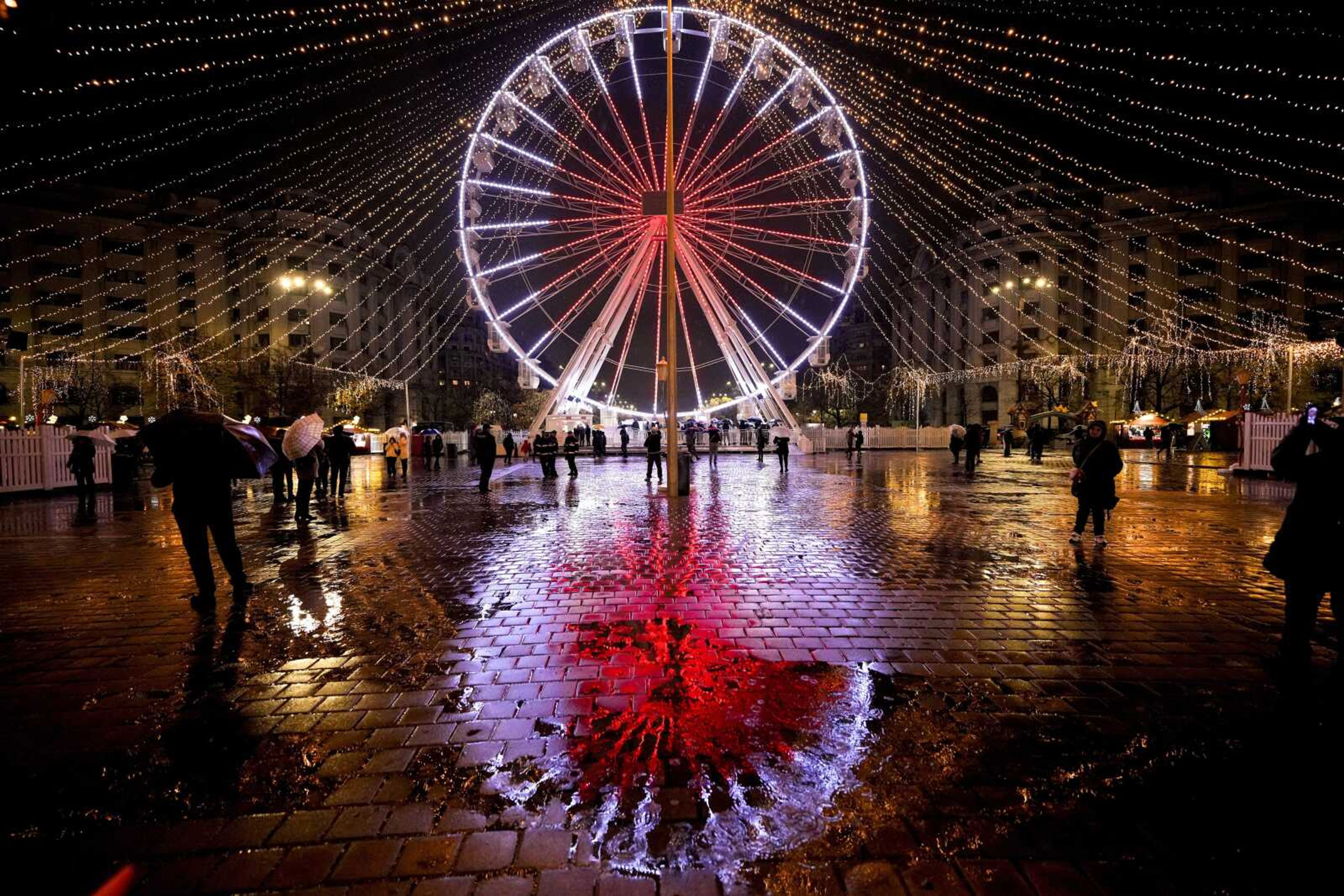 An illuminated Ferris wheel is reflected in the wet pavement at a Christmas fair that opened ahead of the holiday season Nov. 20 in Bucharest, Romania.