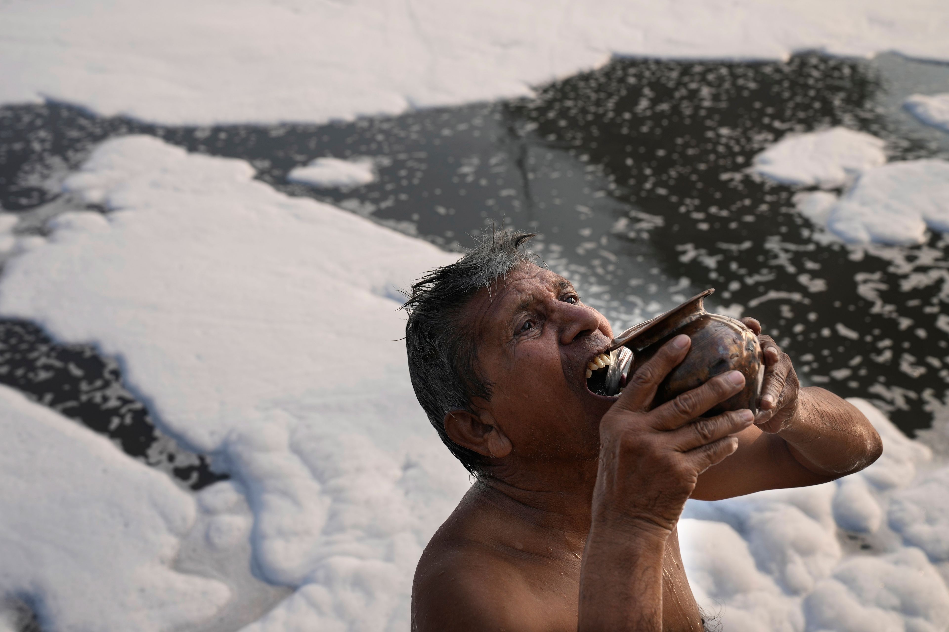 Jasraj, 70, drinks water from the river Yamuna filled with toxic foams in New Delhi, India, Tuesday, Oct. 29, 2024. (AP Photo/Manish Swarup)