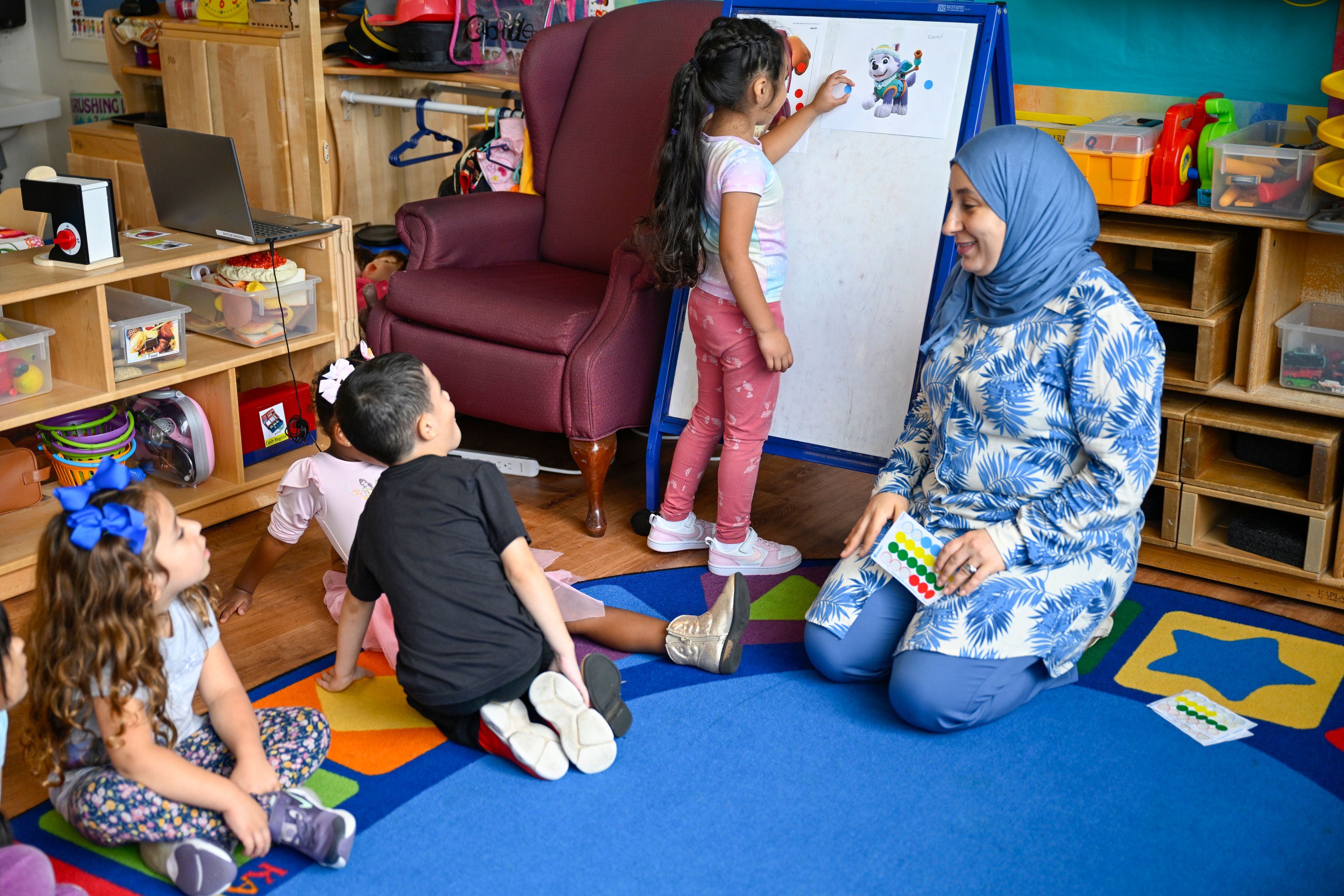 Preschool teacher Tinhinane Meziane, right, watches her students vote the most popular character of the TV show PAW Patrol at the ACCA Child Development Center, Thursday, Sept. 19, 2024, in Annandale, Va. The students are getting foundational lessons on how to live in a democracy by allowing them to regularly vote on different things through out the day. (AP Photo/John McDonnell)