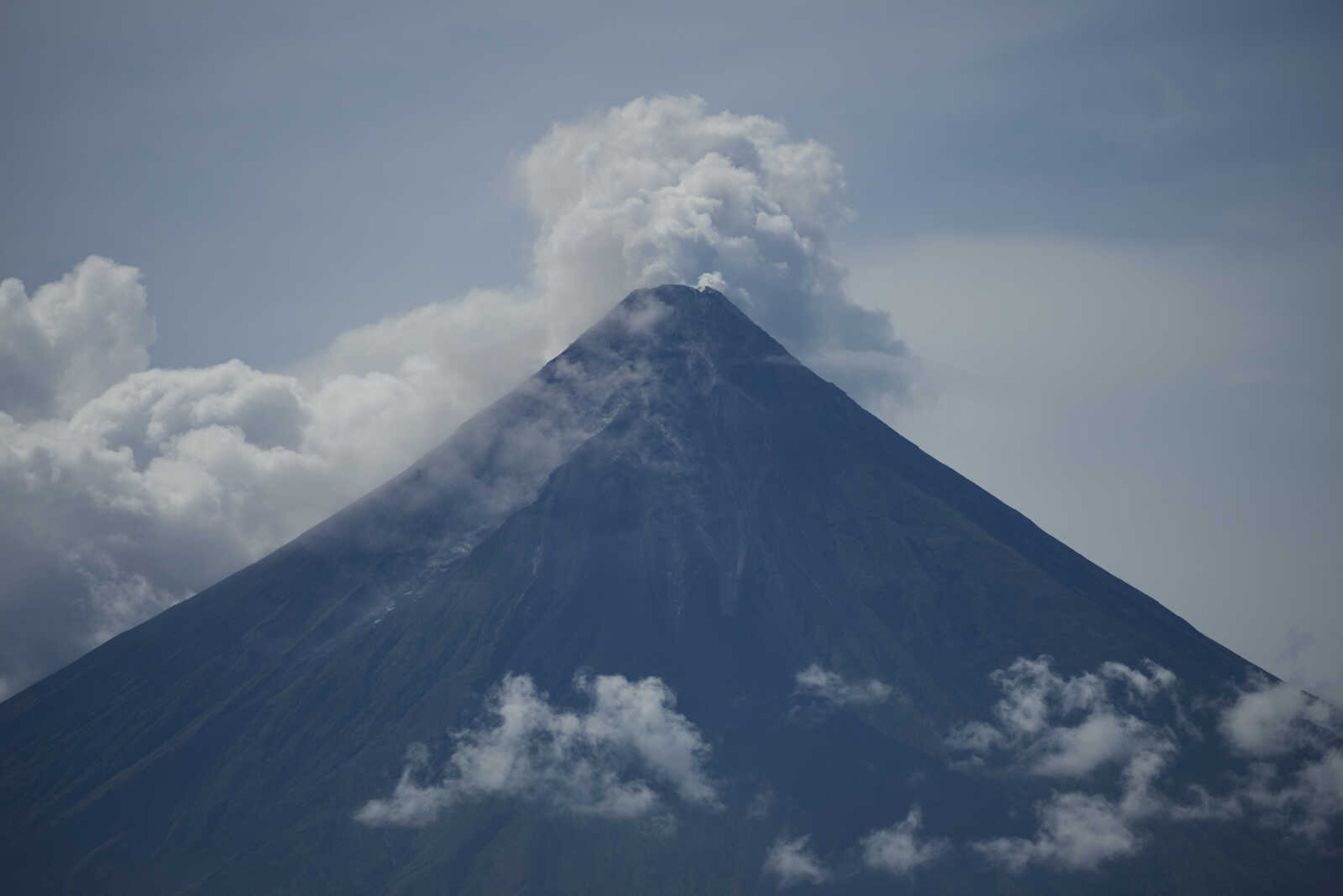 Mayon volcano spews white smoke as seen from a government declared permanent danger zone at Malilipot, Albay province, northeastern Philippines, on June 15, 2023. Thousands of poor Filipinos risk their lives by living and working in villages inside a permanent danger zone around Mayon volcano. (AP Photo/Aaron Favila)