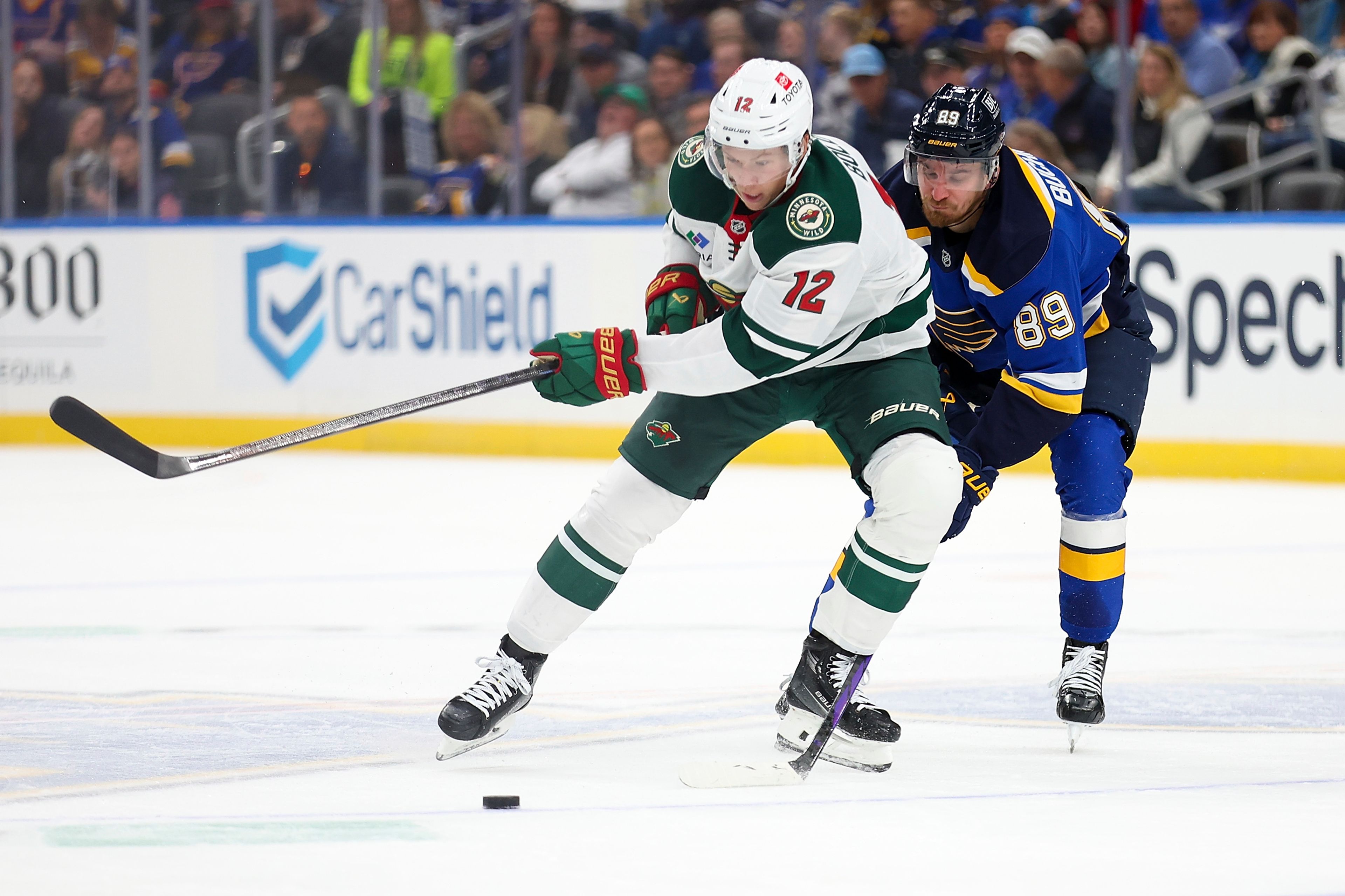 Minnesota Wild's Matt Boldy (12) and St. Louis Blues' Pavel Buchnevich (89) vie for control of the puck during the first period of an NHL hockey game Tuesday, Oct. 15, 2024, in St. Louis. (AP Photo/Scott Kane)