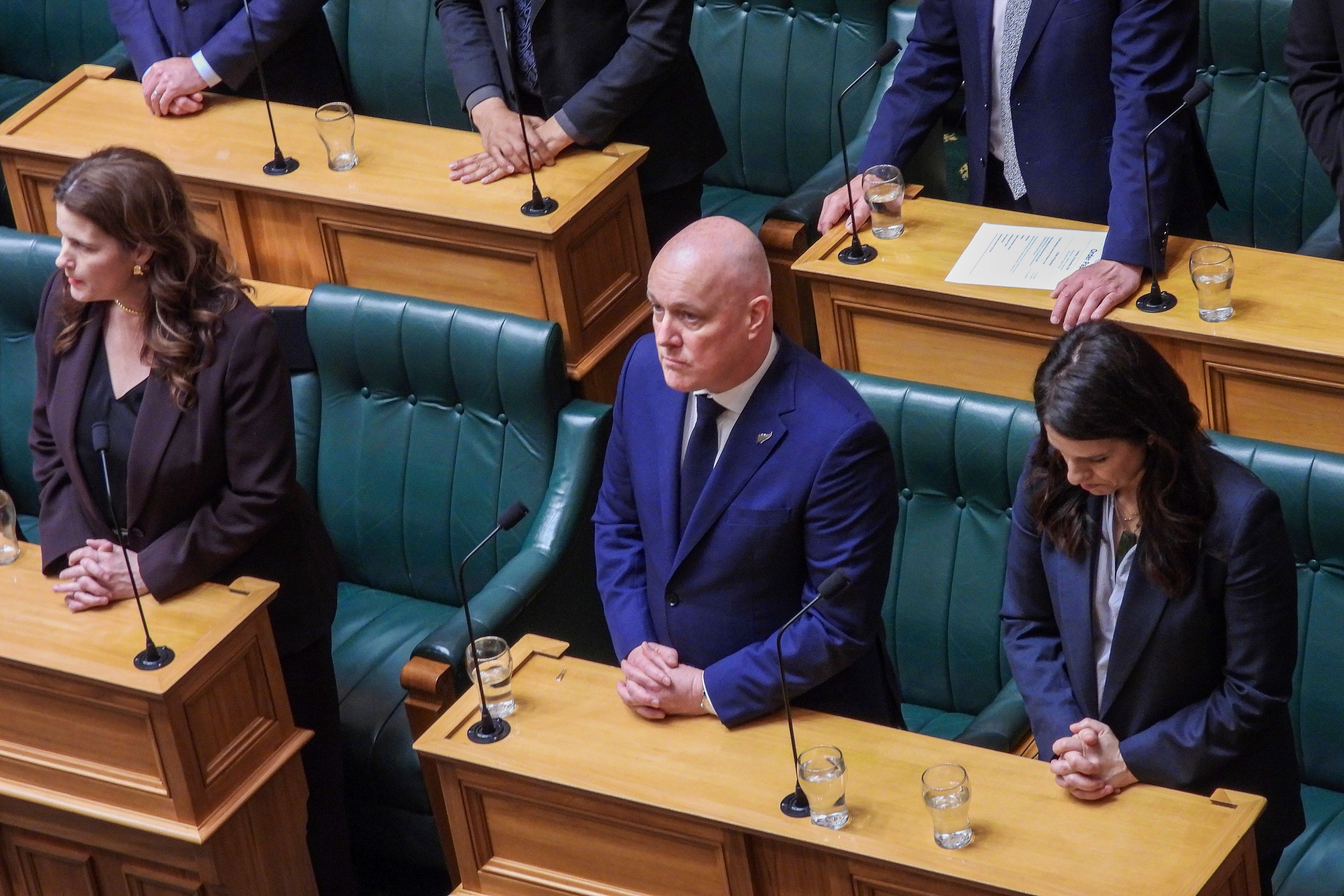 New Zealand Prime Minister Christopher Luxon, center, stands in silence ahead of making a "formal and unreserved" apology in Parliament for the widespread abuse, torture and neglect of hundreds of thousands of children and vulnerable adults in care, in Wellington, New Zealand Tuesday, Nov. 12, 2024. (AP Photo/Charlotte Graham-McLay )