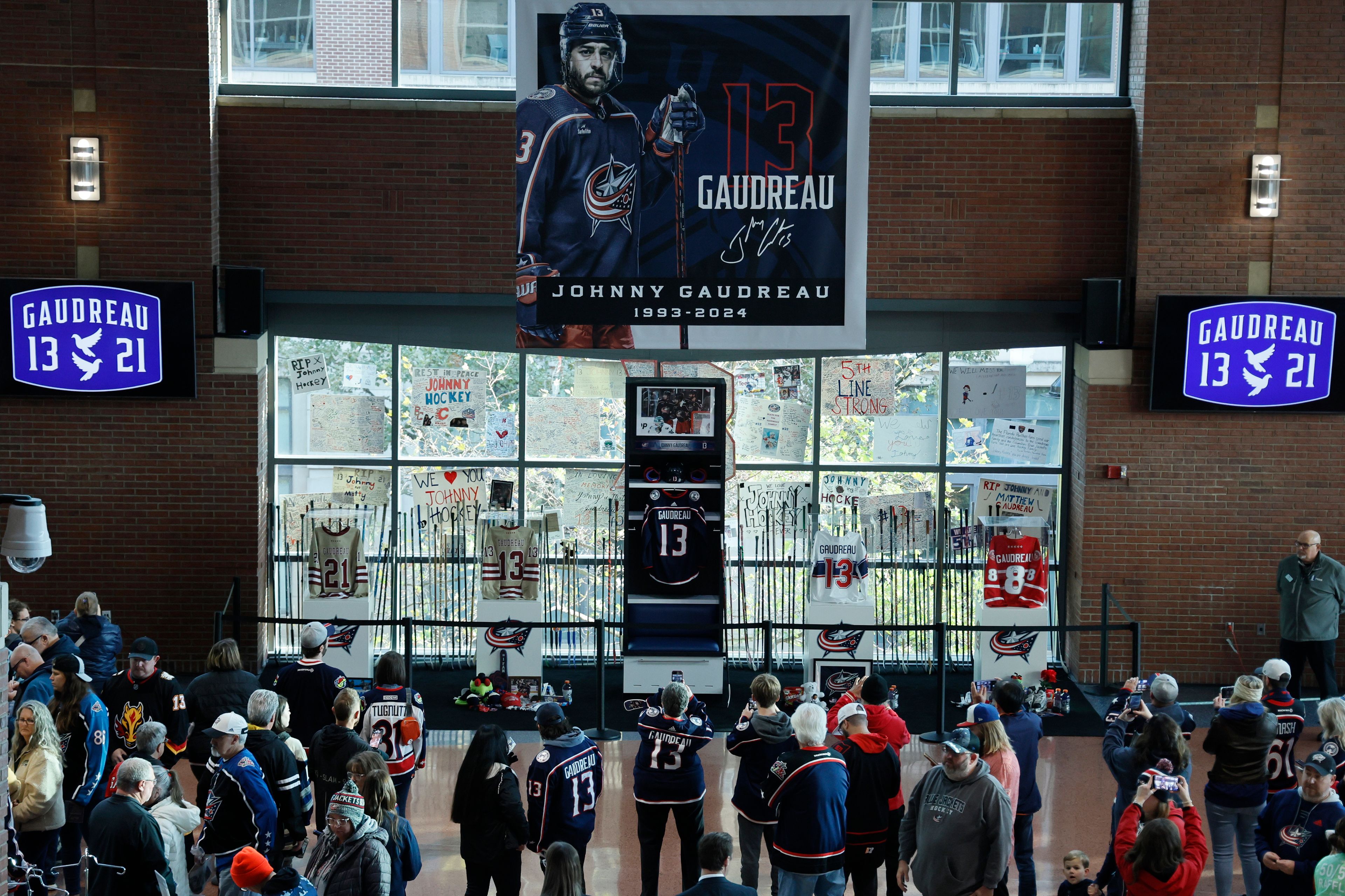 Fans look at a memorial of Columbus Blue Jackets' Johnny Gaudreau and his brother Matthew before the start of an NHL hockey game against the Florida Panthers. Tuesday, Oct. 15, 2024, in Columbus, Ohio. (AP Photo/Jay LaPrete)