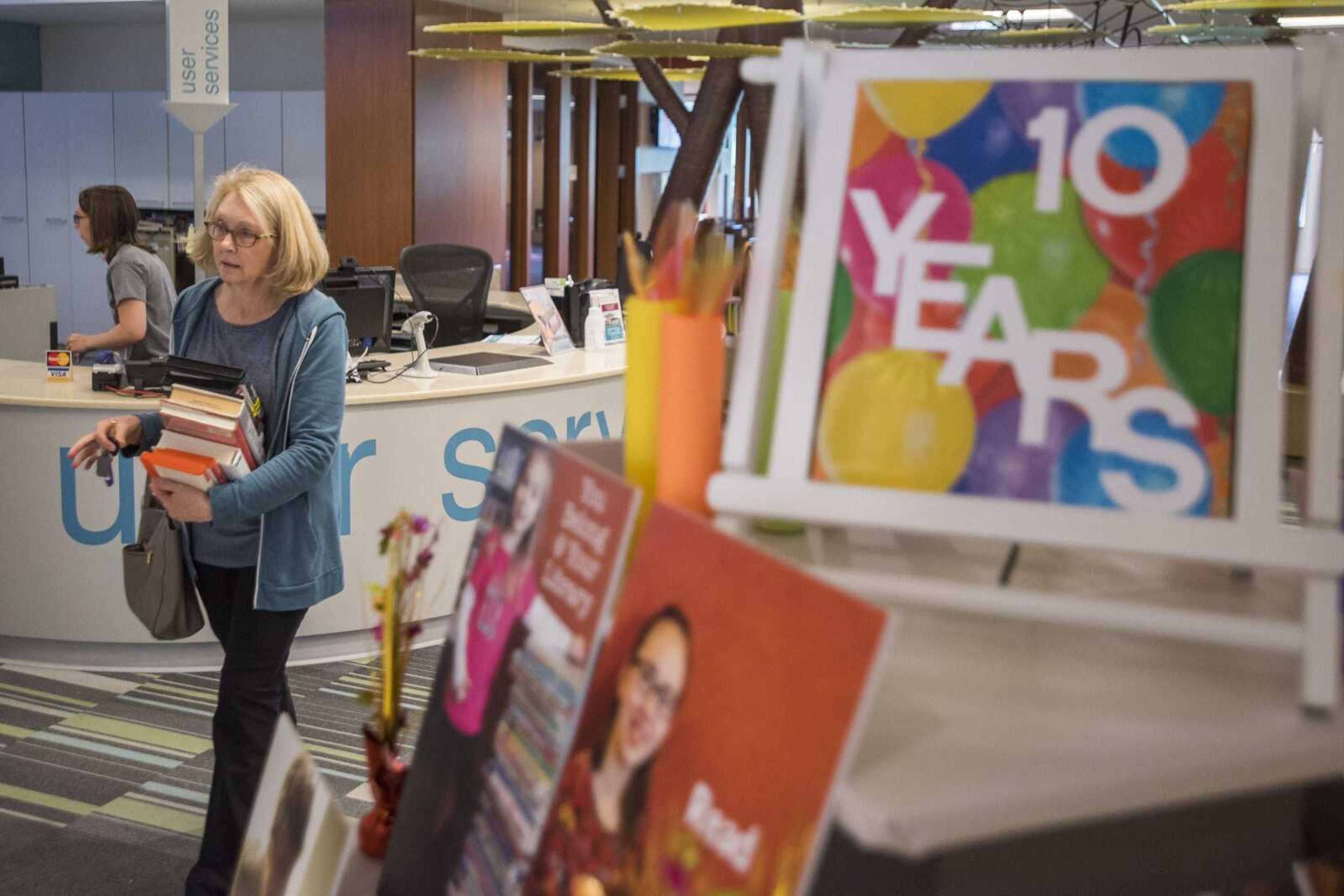 Debra Bader carries a stack of books past a display celebrating the library's 10th anniversary Wednesday at the Cape Girardeau Regional Library.