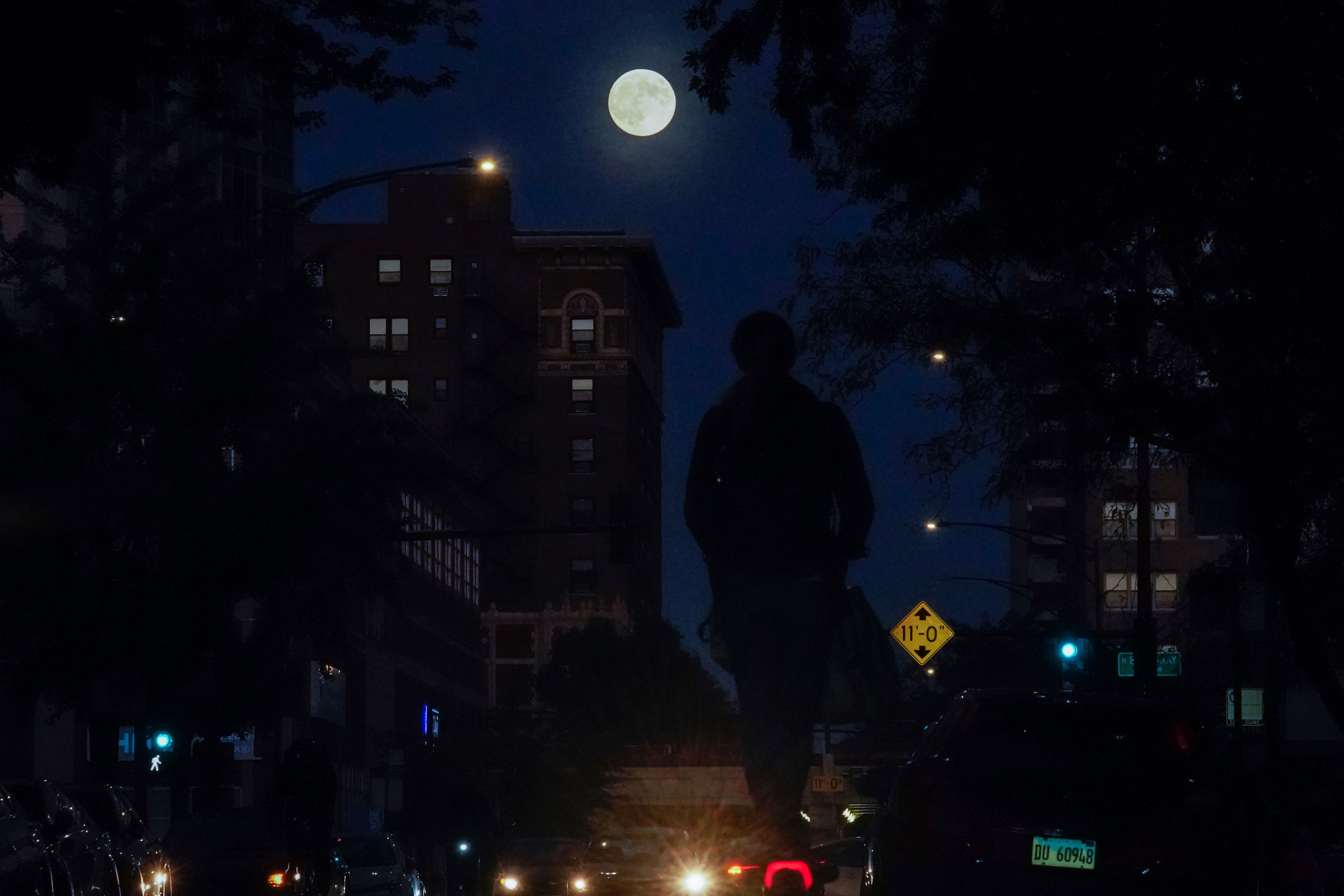 The full moon rises as a person cruises down a street on an electric scooter Wednesday, Oct. 16, 2024, in Chicago. (AP Photo/Kiichiro Sato)