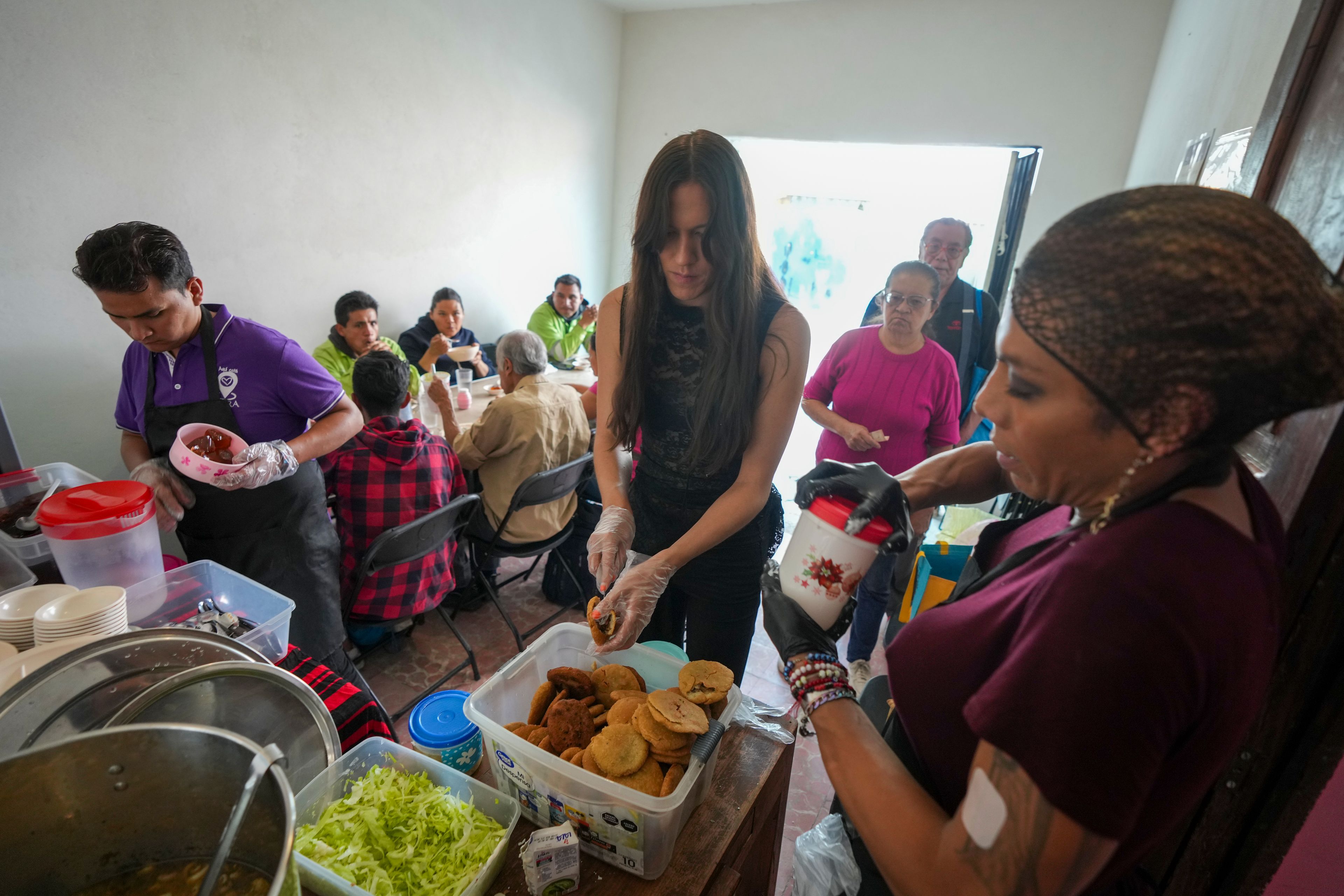 Victoria Sámano, center, Karolina Long Tain González Rodríguez, right, and Yamileth Adriano — all trans women — serve meals at Casa Lleca, the LGBTQ+ shelter they operate in the Peralvillo neighborhood of Mexico City, Friday, Sept. 20, 2024. Samano founded the shelter in 2020 in an effort to help LGBTQ+ people and sex workers who were unhoused or at risk of losing their homes. (AP Photo/Fernando Llano)