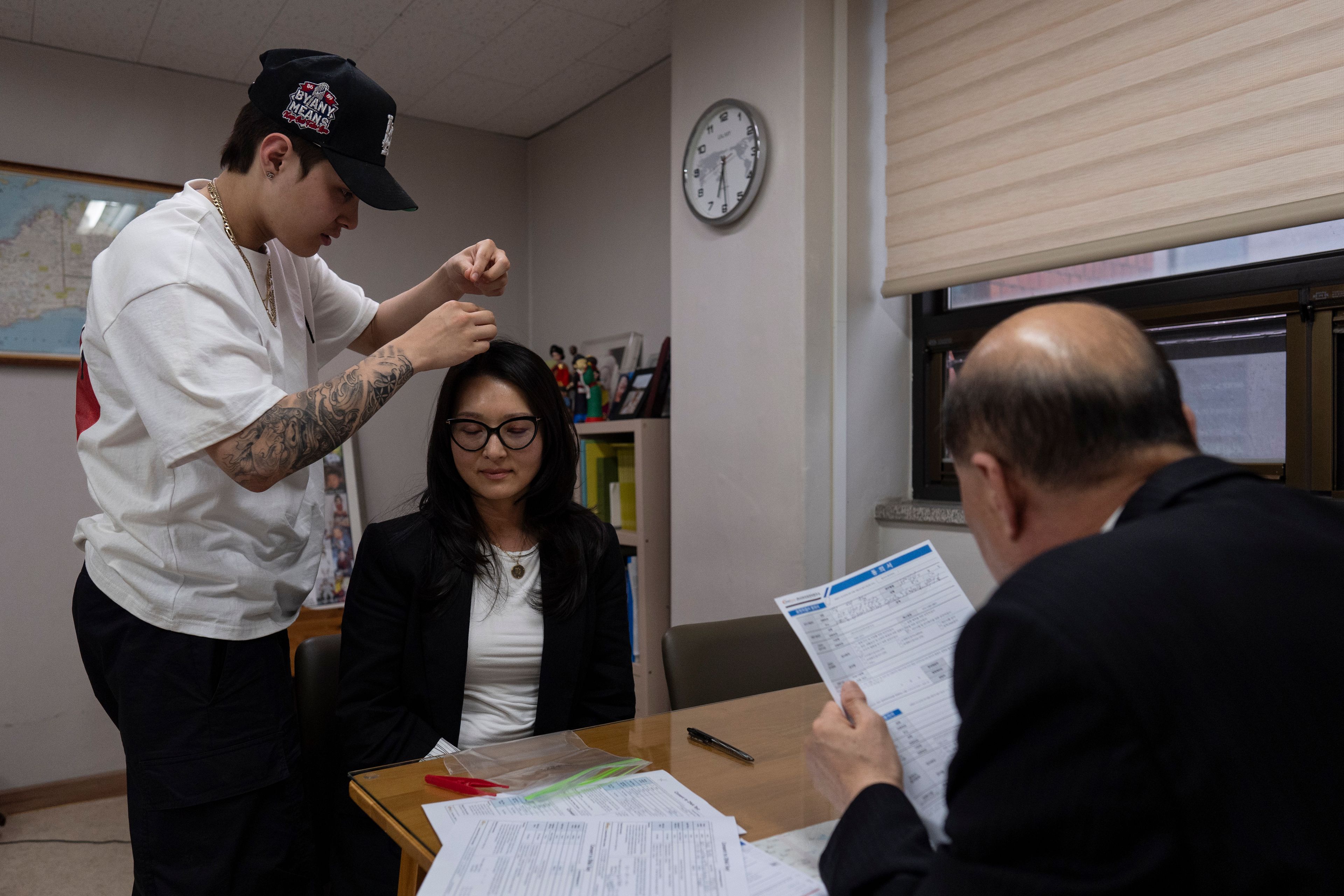 Nicole Motta's son, Adler, collects hair samples from his mother for a DNA test as her birth father, Jang Dae-chang, reviews the paperwork at the Eastern Social Welfare Society in Seoul, South Korea, Friday, May 31, 2024. The two were reunited for the first time since she was adopted by a family in Alabama, United States, in 1985. (AP Photo/Jae C. Hong)