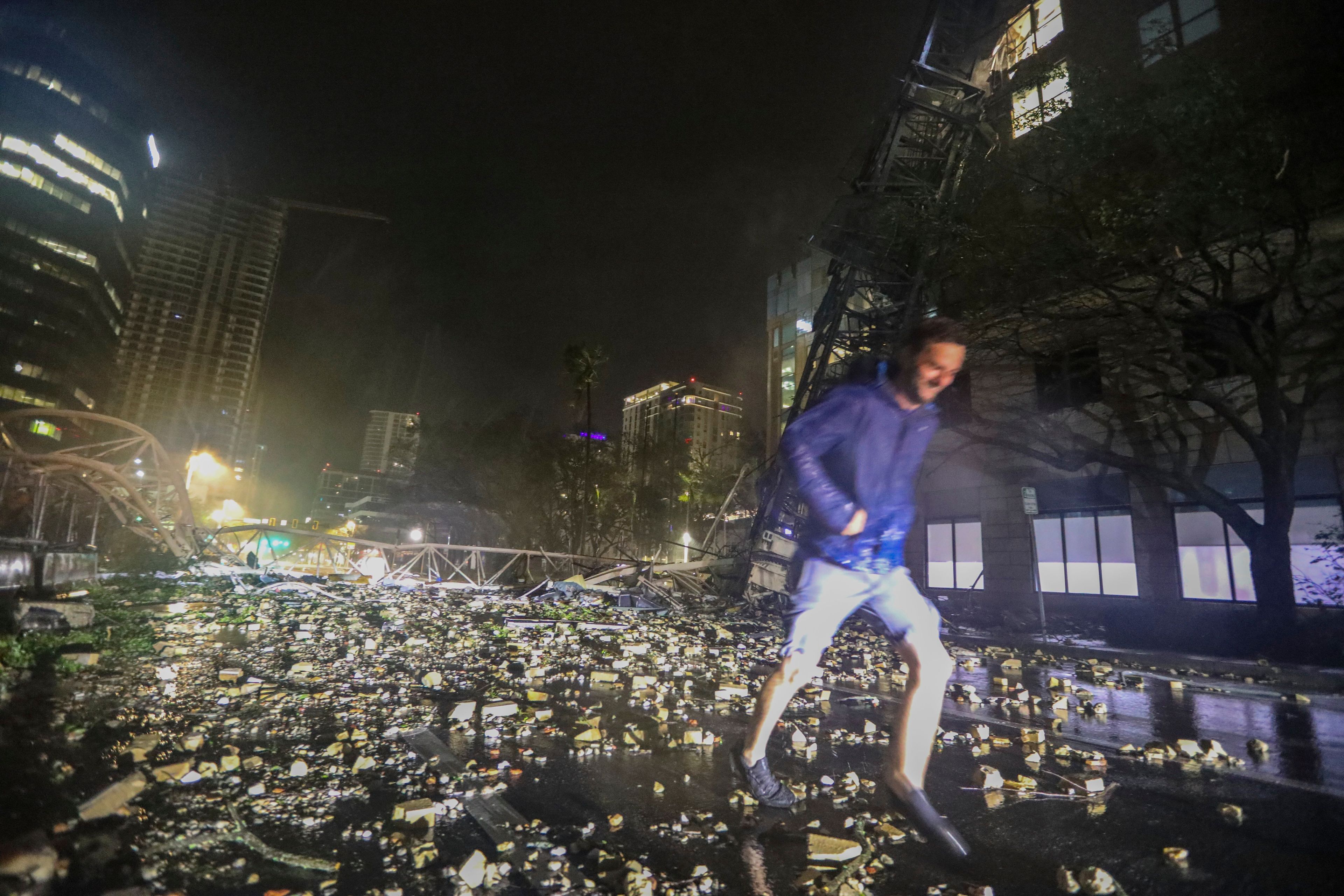 Joe Lindquist, 32, of St. Petersburg, walks over bricks near a fallen crane along 1st Avenue South near the Tampa Bay Times offices in St. Petersburg, Florida, Thursday, Oct. 10, 2024, as Hurricane Milton's strong winds tore through the area. (Chris Urso/Tampa Bay Times via AP)