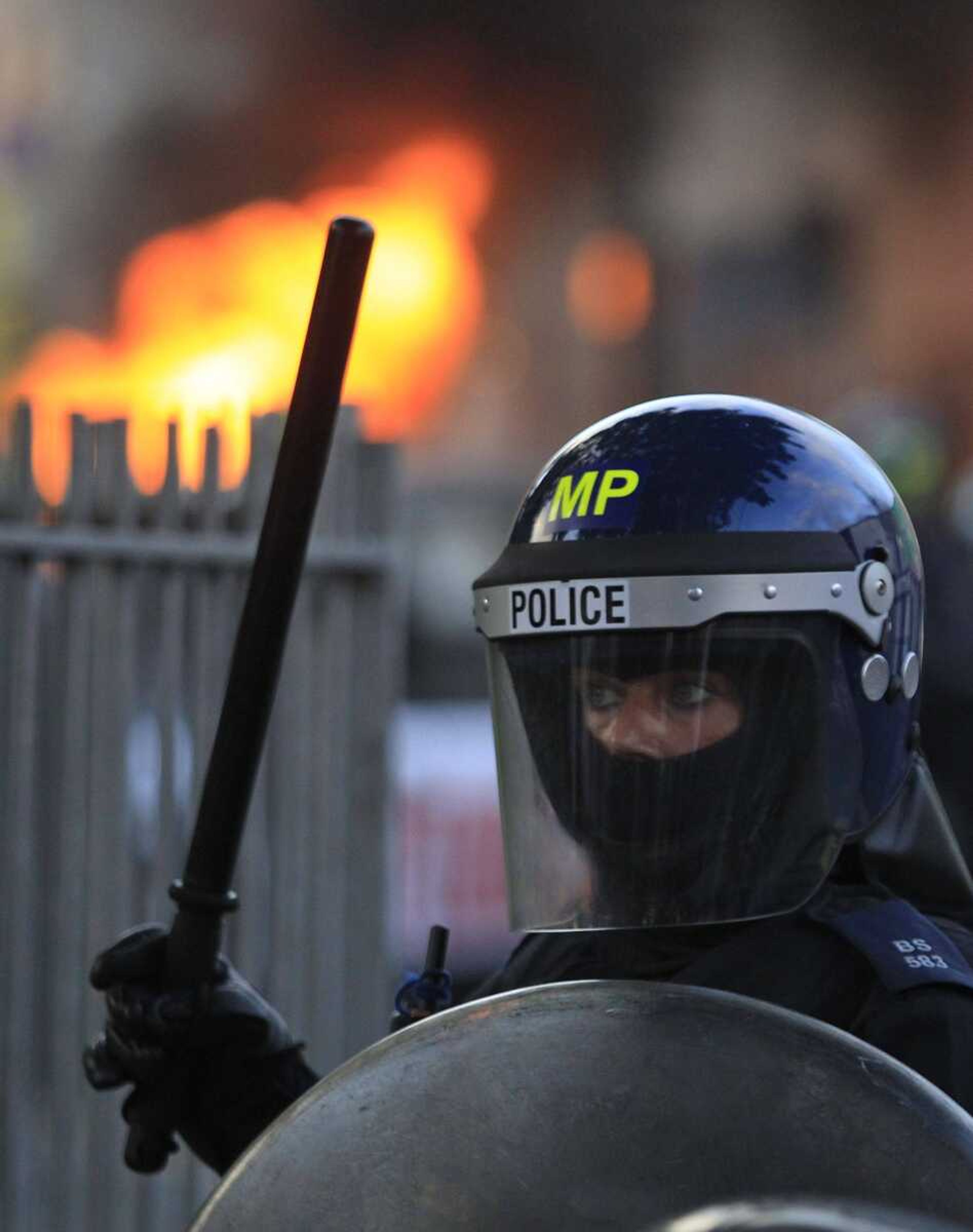 A British police officer stands guard Aug. 8 as a car burns in east London. (Lefteris Pitarakis ~ Associated Press)