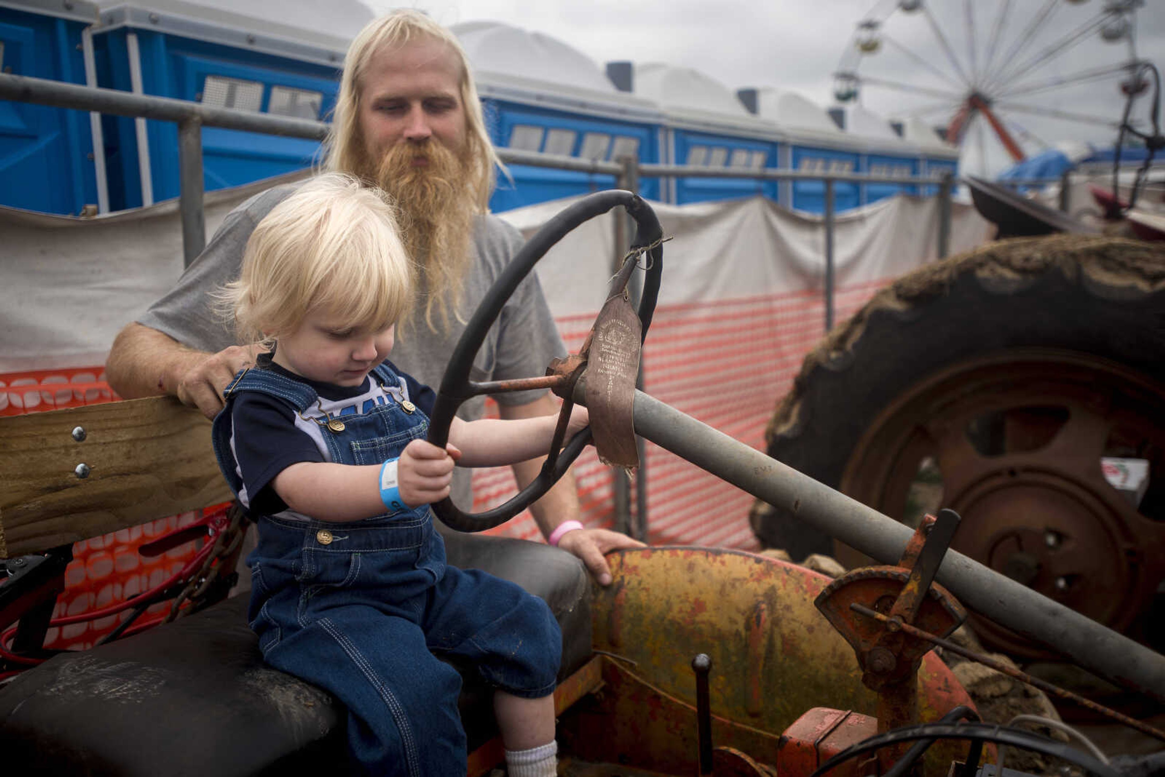 Eric Mayberry watches his 2-year-old son, Holland, play on a tractor before the start of the demolition derby Sunday. Mayberry, as a member of the Egypt Mills Antique Tractor Club, has helped drag broken derby cars off the arena for the last decade.