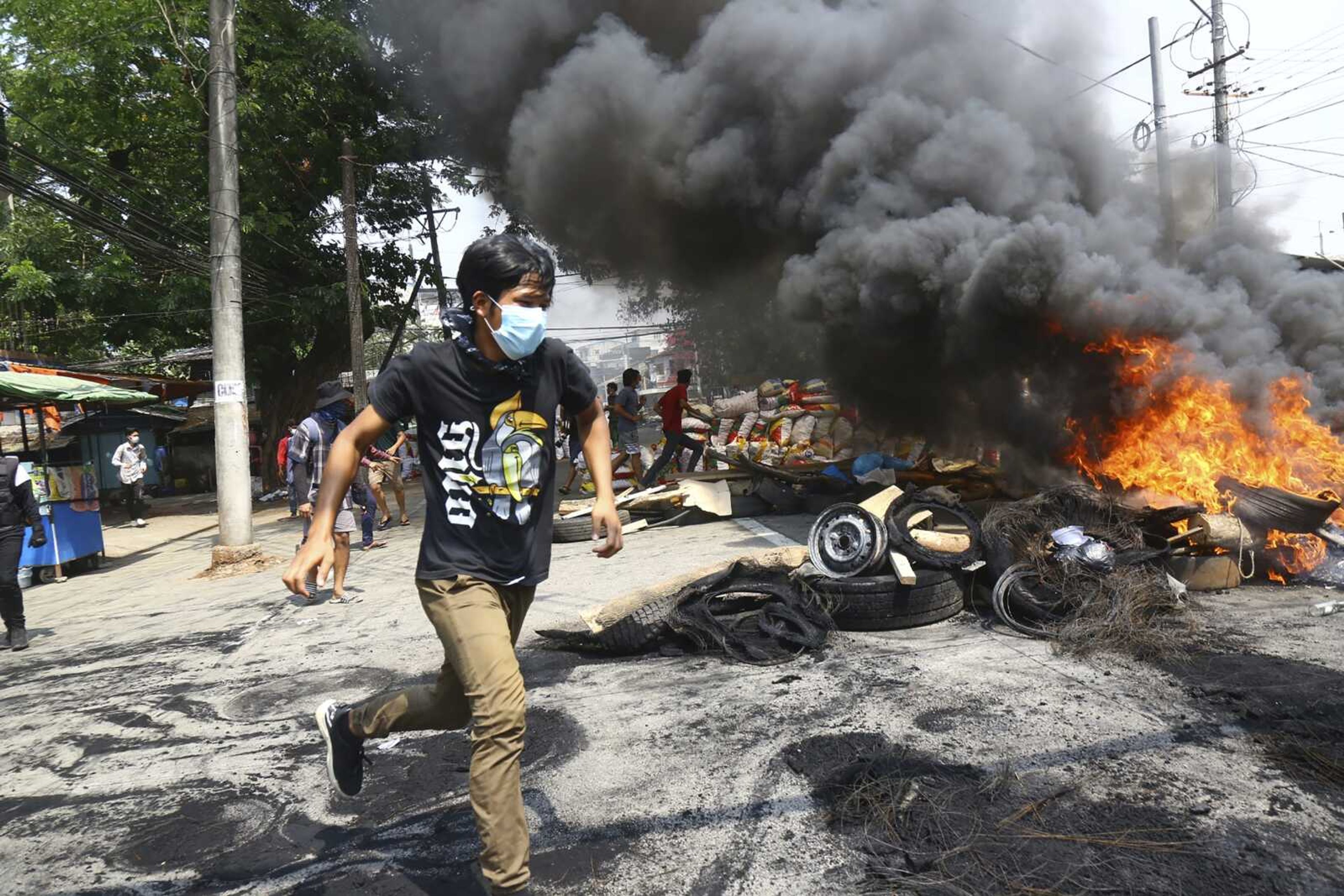 Anti-coup protesters run around their makeshift barricade they burn to make a defense line during a demonstration Sunday in Yangon, Myanmar. Protesters in Myanmar returned to the streets Sunday to press their demands for a return to democracy, just a day after security forces killed more than 100 people in the bloodiest day since last month's military coup.