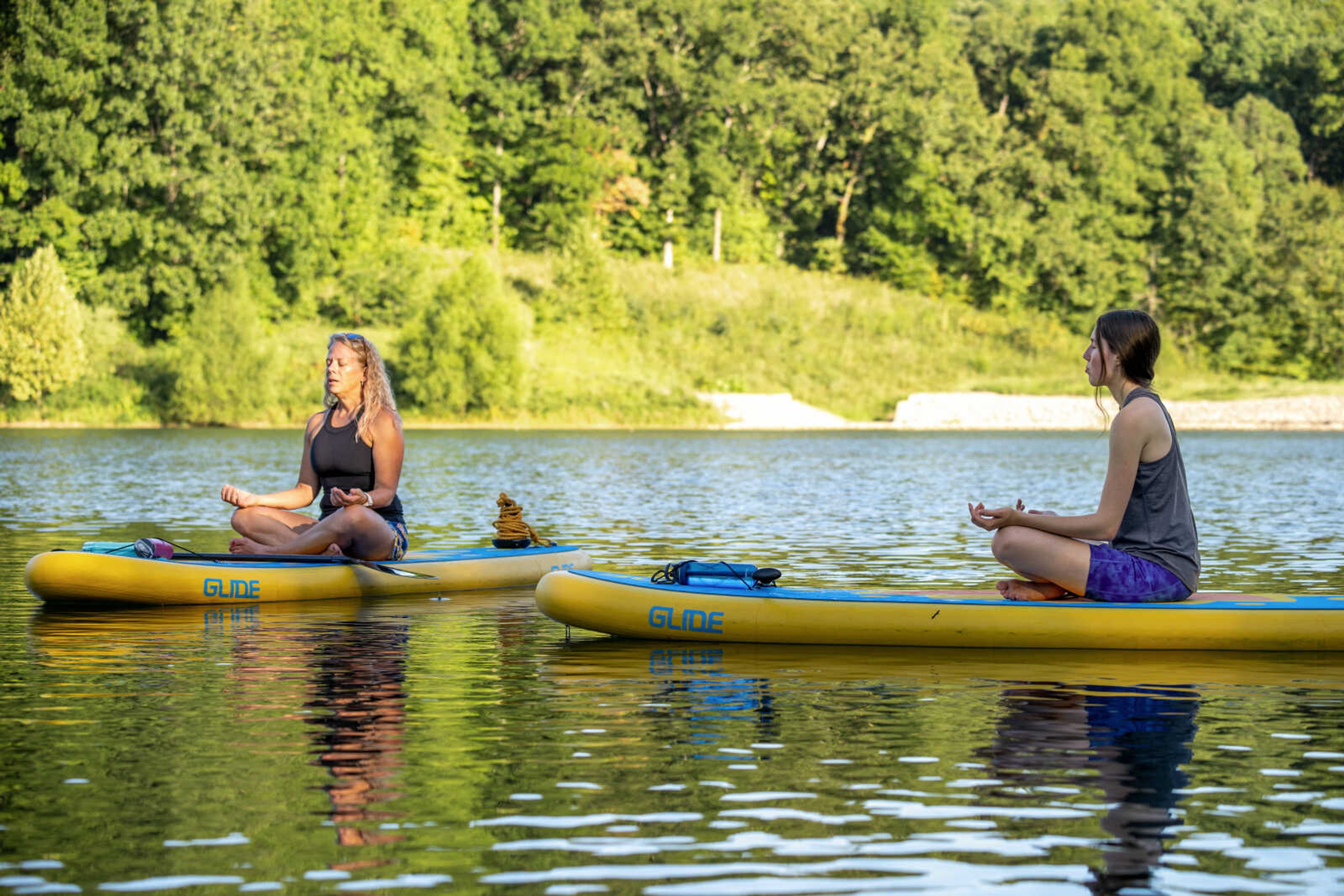 Missy Nieveen Phegley (left) leads a stand up paddleboard (SUP) yoga class in guided relaxation. Jasmine Jones participates.