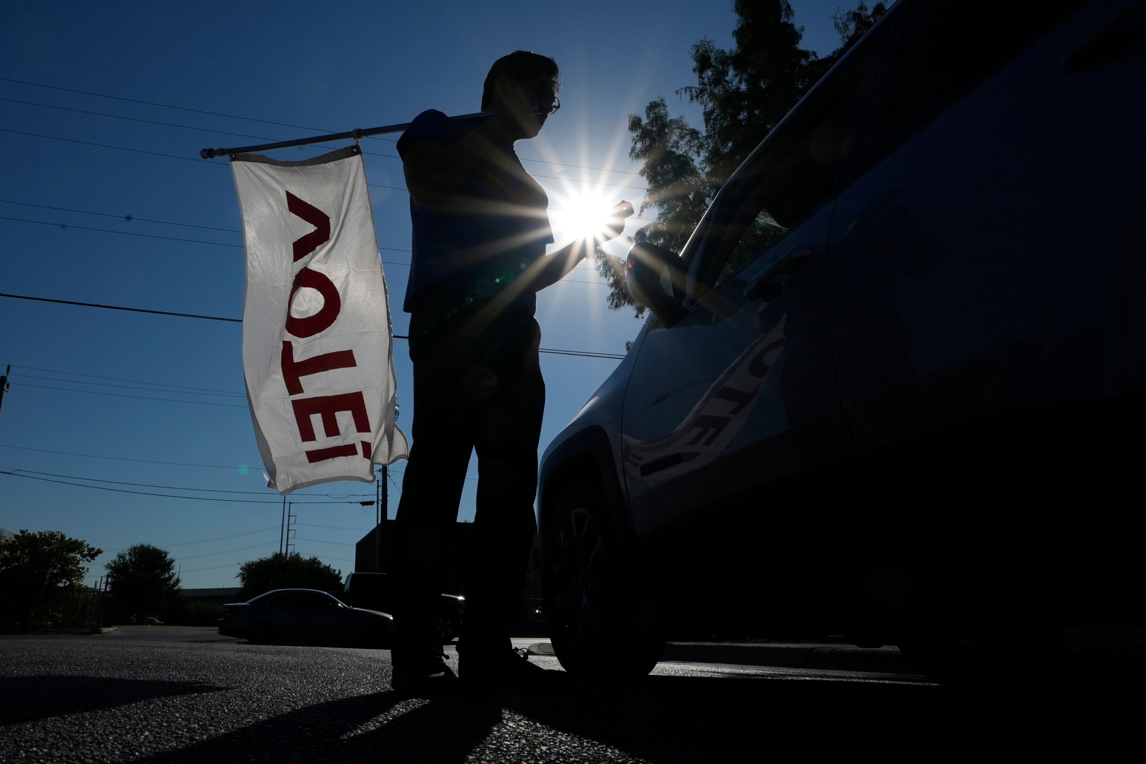 Artist David Alcantar holds a "VOTE" flag as he gives directions to a motorist outside the Bexar County Elections Department in San Antonio, Tuesday, Oct. 15, 2024. (AP Photo/Eric Gay)