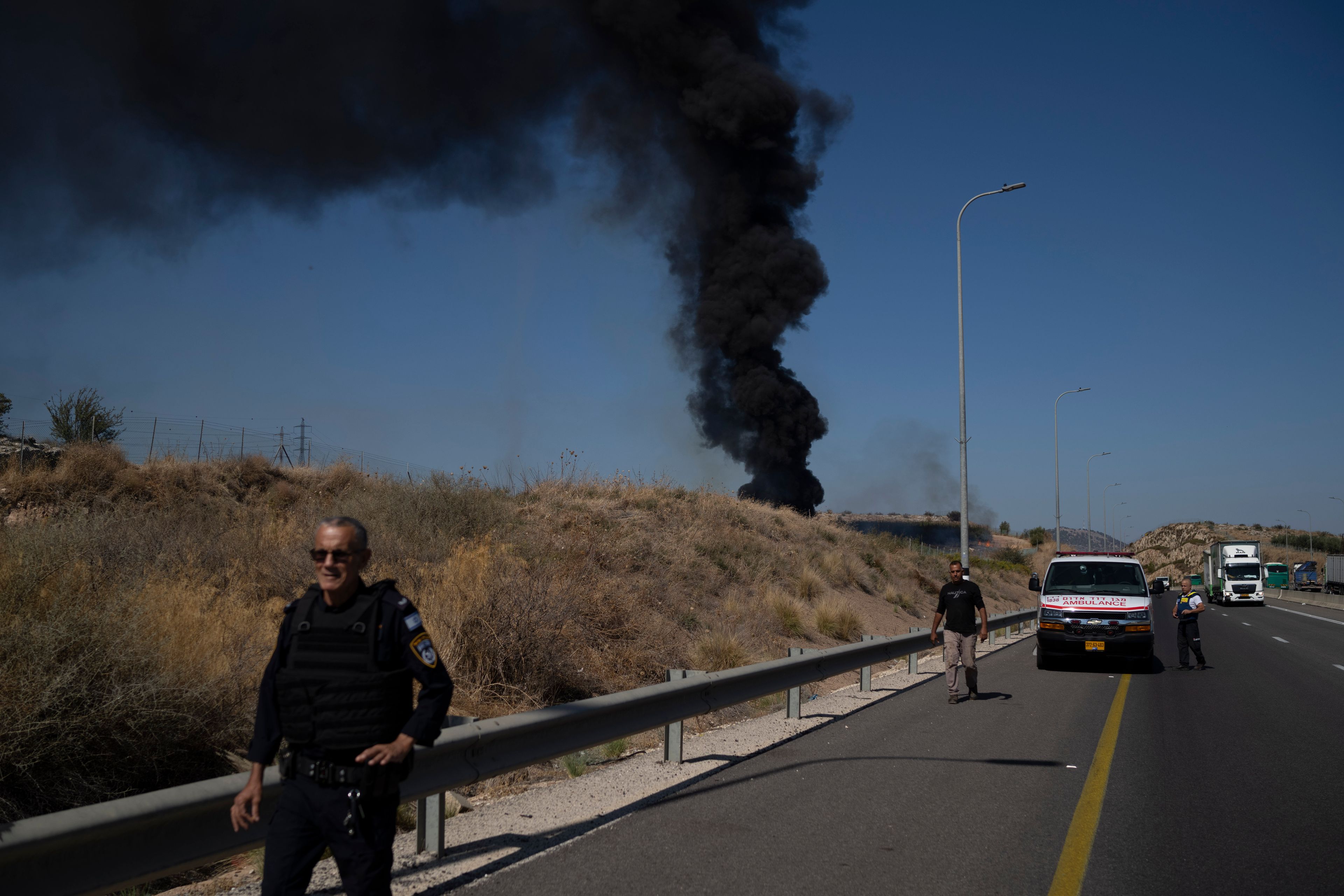 A Israeli police officer walks past site of a fire after a rocket, fired from Lebanon, hit an area near the town of Rosh Pinna, northern Israel, Sunday, Oct. 20, 2024. (AP Photo/Leo Correa)