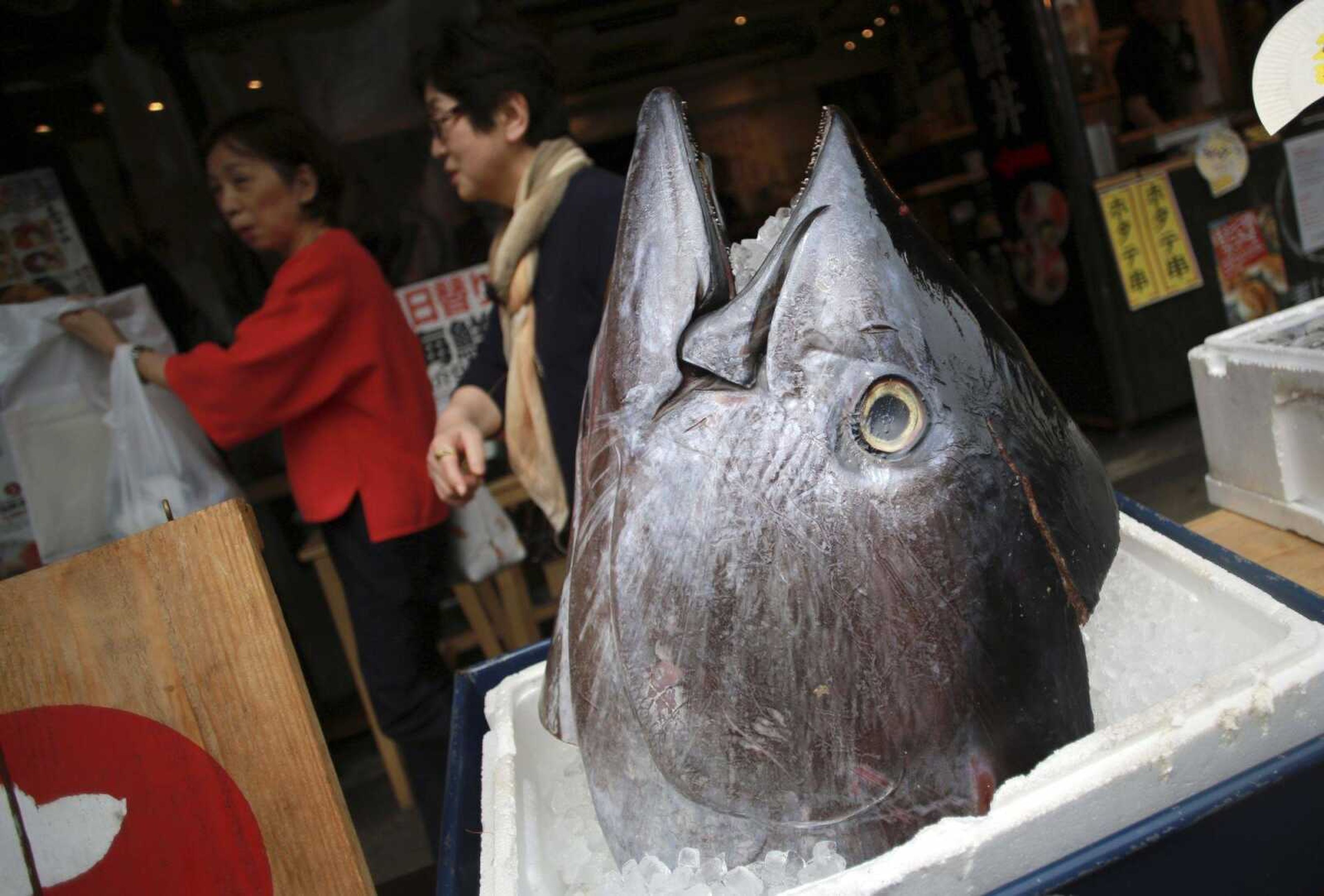 Customers walk past the head of a bluefin tuna in front of a seafood restaurant Tuesday at Tsukiji fish market in Tokyo.