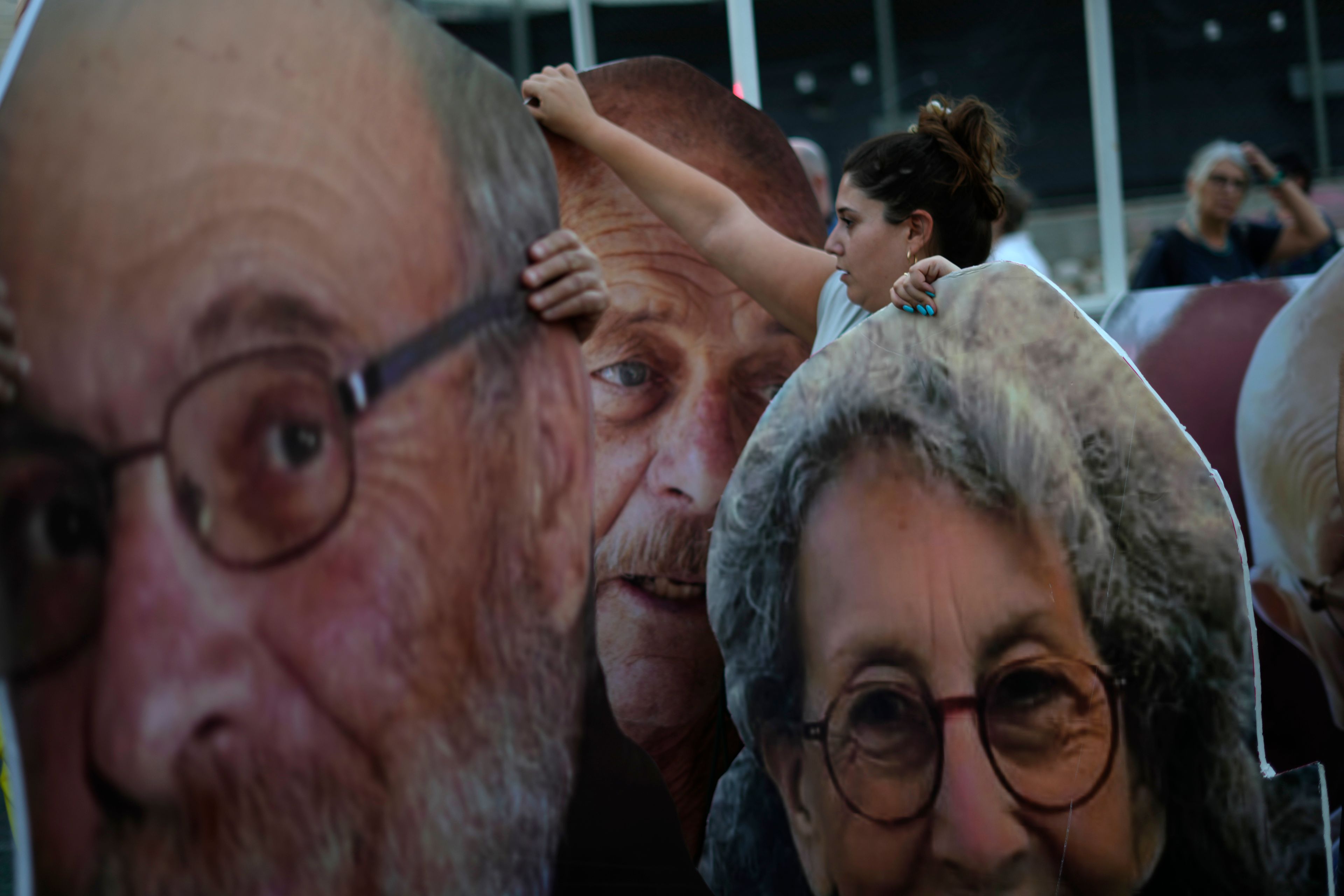 A protester stands with large cutout photos of slain hostages Yoram Metzger, left, and Haim Peri, center, with hostage Judi Weinstein Haggai, right, as relatives of hostages taken by Hamas militants to the Gaza Strip to honor the memories of six men whose bodies were returned and to call for a deal to release the remaining captives, in Tel Aviv, Tuesday, Aug. 20, 2024. (AP Photo/Ariel Schalit)