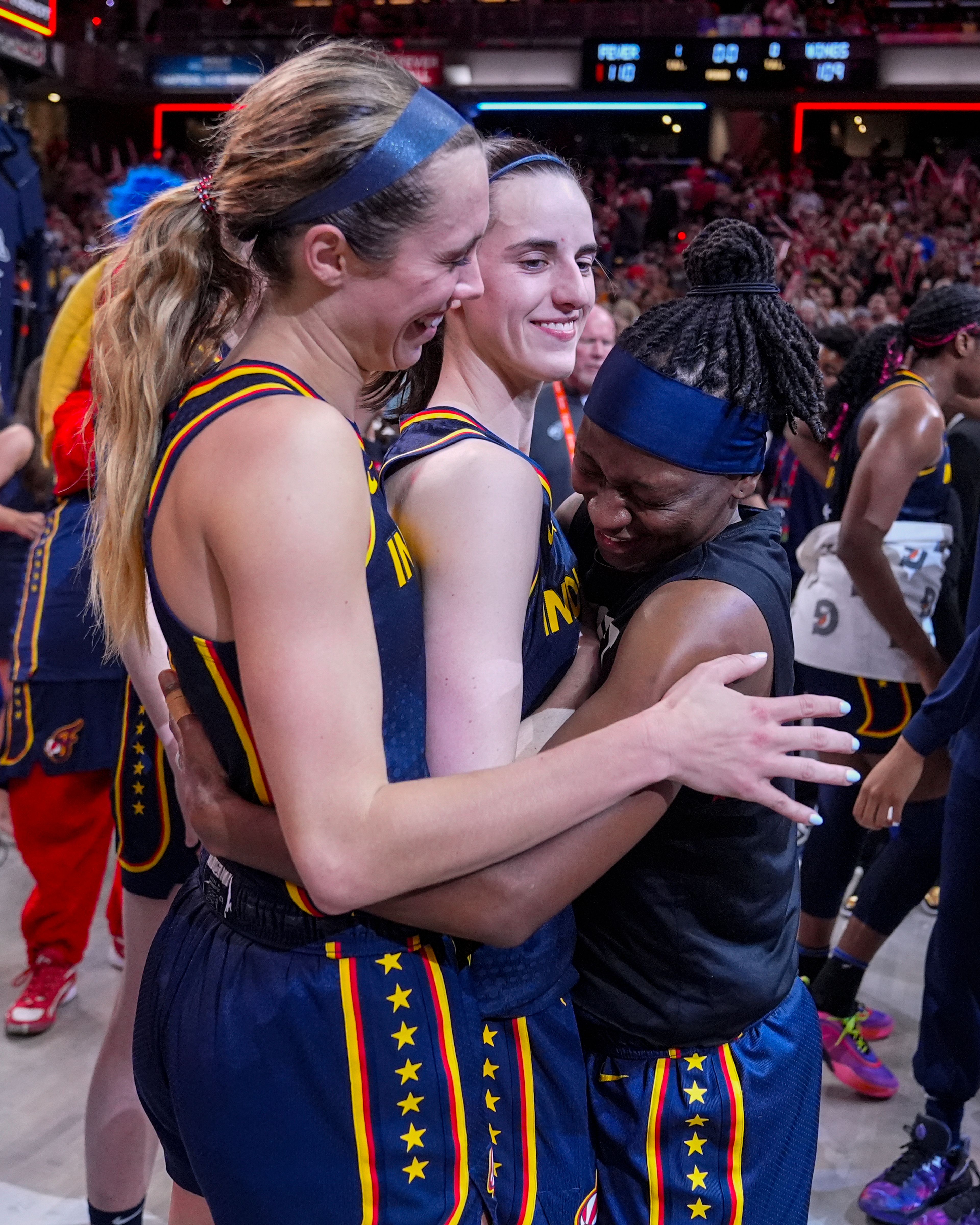 Indiana Fever guard Caitlin Clark, center is hugged by Lexie Hull, left, and Erica Wheeler (17) after a WNBA basketball game against the Dallas Wings in Indianapolis, Sunday, Sept. 15, 2024. (AP Photo/Michael Conroy)