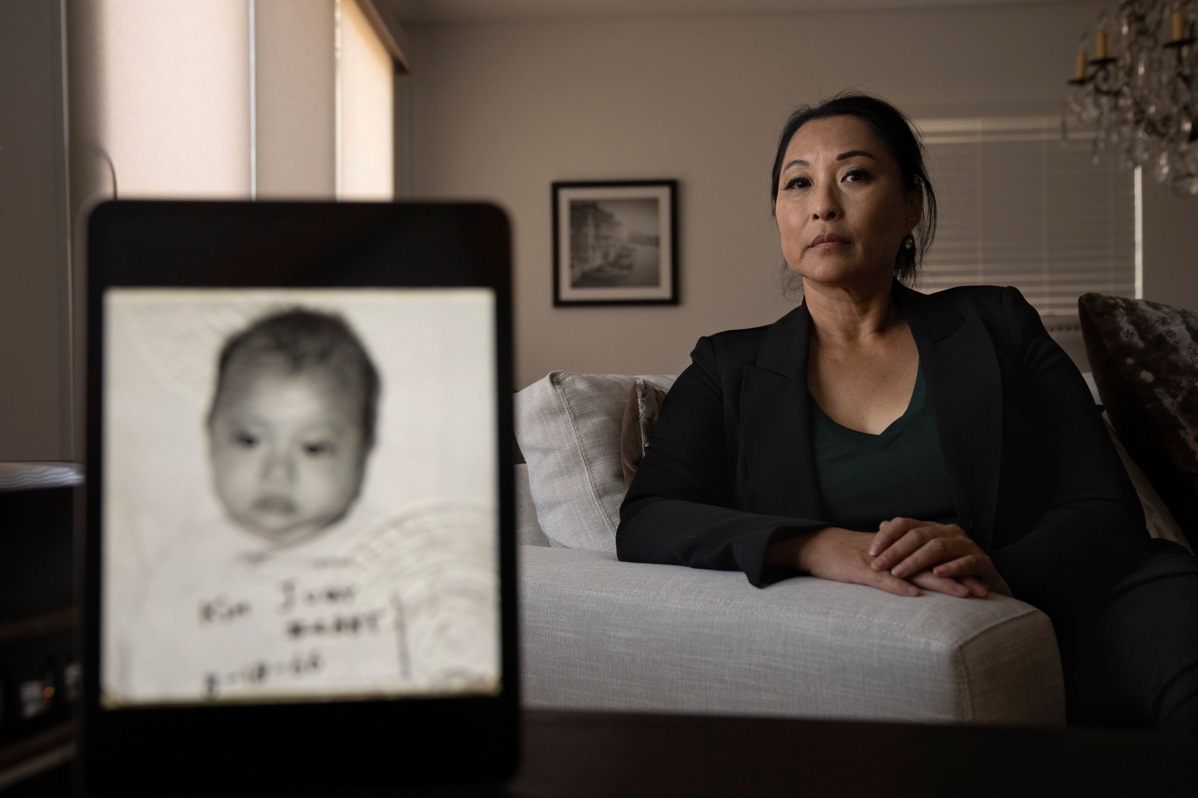 Joy Alessi sits for a portrait behind her baby picture from before she was adopted from South Korea to a family in America, Tuesday, June 25, 2024, in Henderson, Nev. (AP Photo/David Goldman)